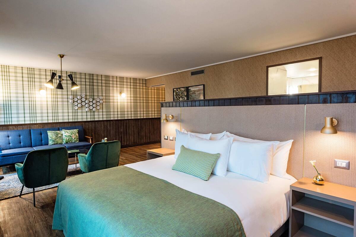 Habitación de hotel con una cama grande, un sofá azul, una mesita pequeña y un espejo montado en la pared.