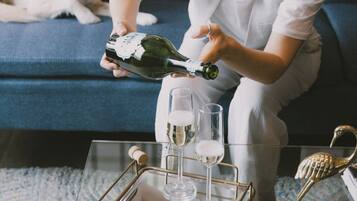A person pouring champagne into glasses on a tray, with a dog on a blue couch in the background.