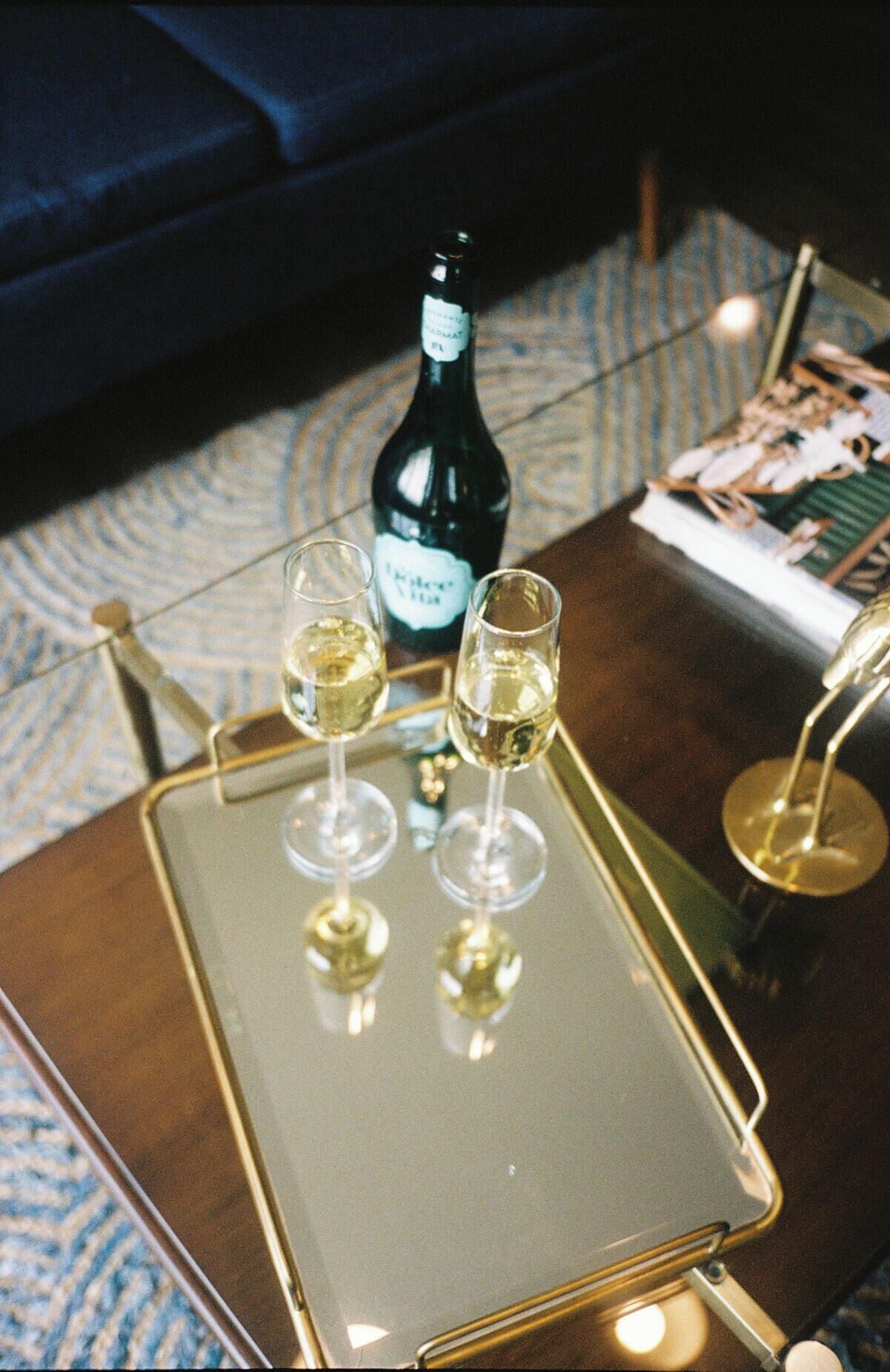 A tray with two glasses of white wine and a bottle of wine on a table.