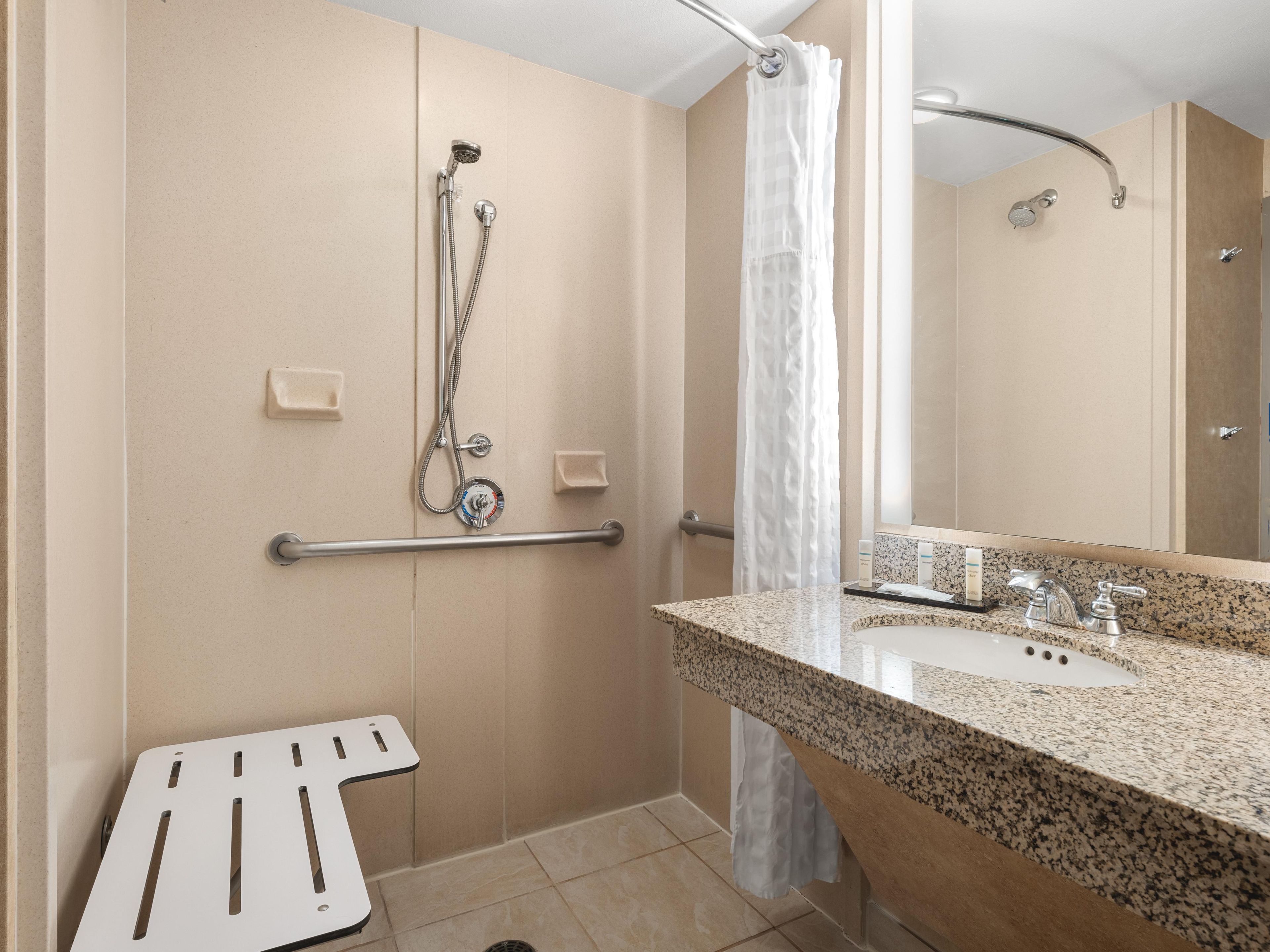 A bathroom with a shower, a grab bar, a sink with a mirror, and a towel rack.