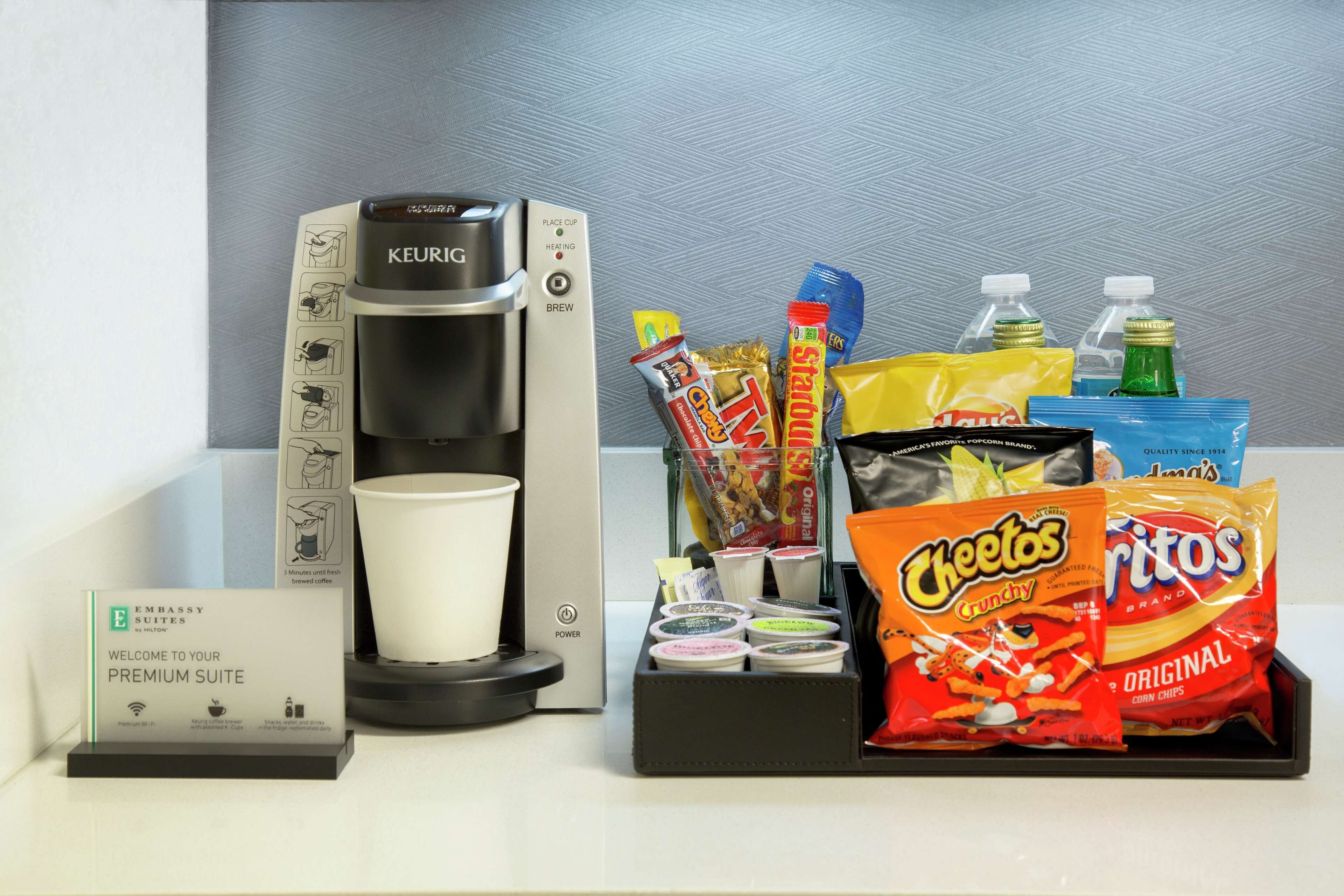 A coffee maker, a cup, and snacks including Cheetos and Doritos.