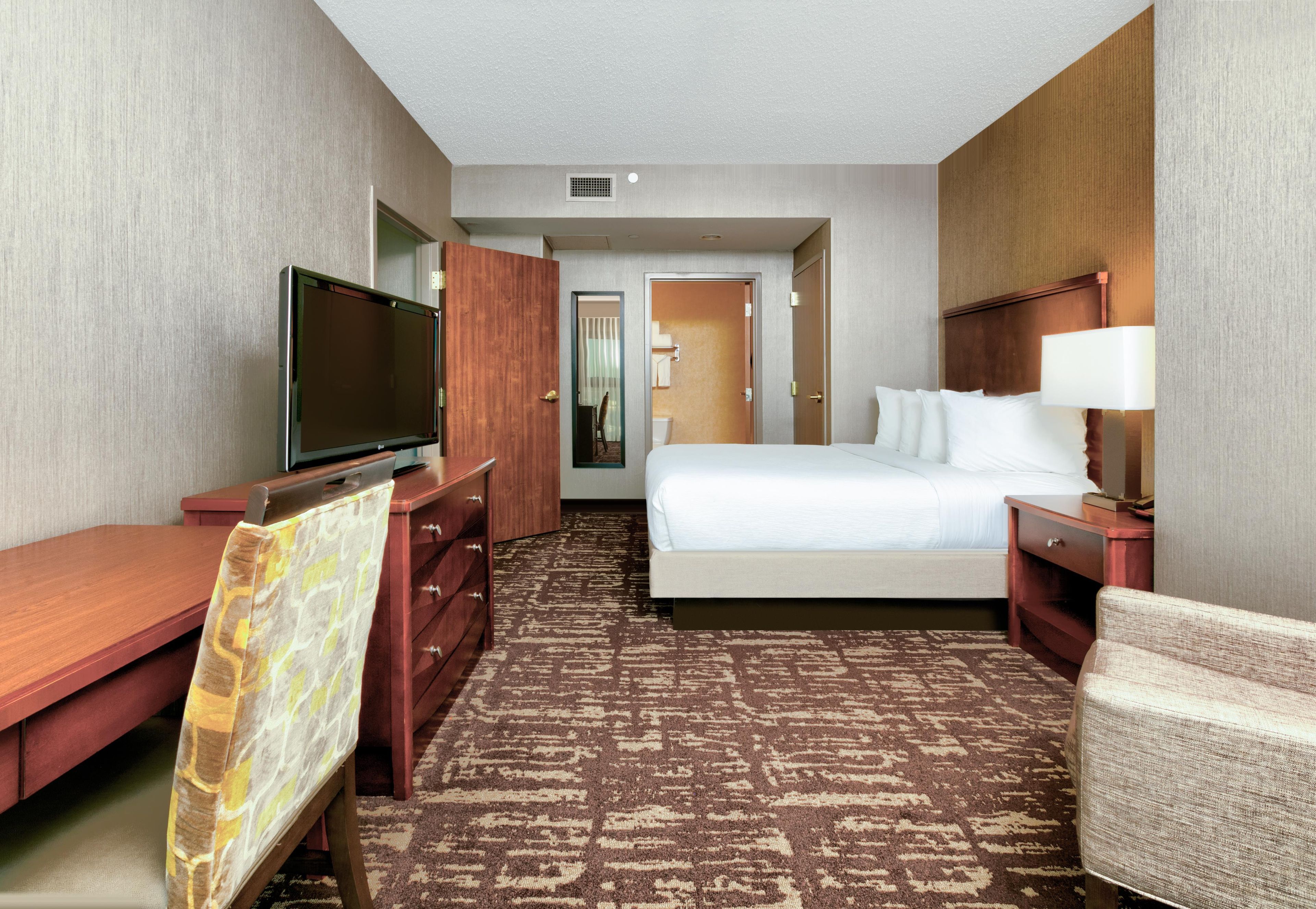 A hotel room with a bed, a desk, a television, a chair, and a carpeted floor.