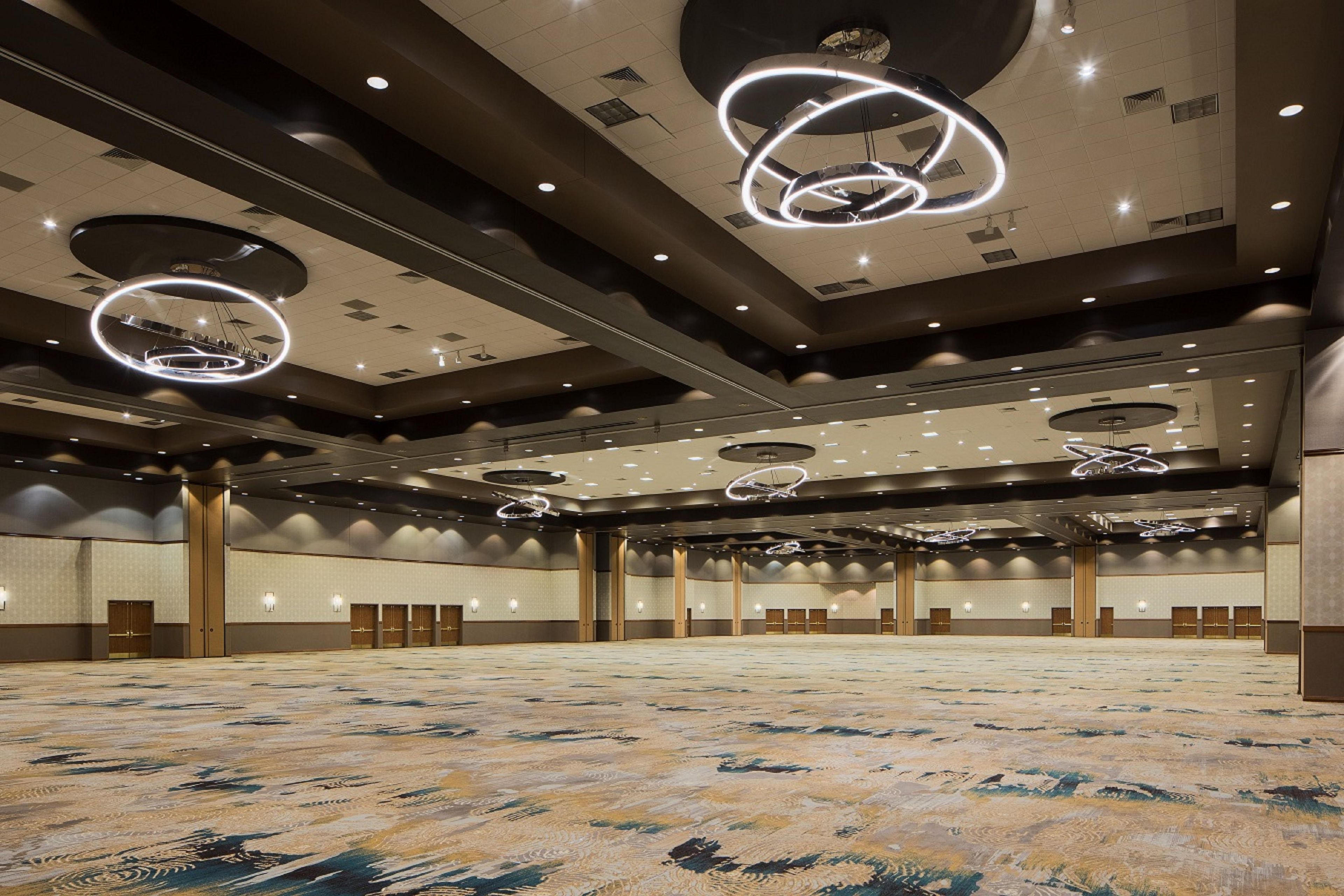 Un amplio vestíbulo de hotel con techo alto, lámparas circulares y alfombra estampada.