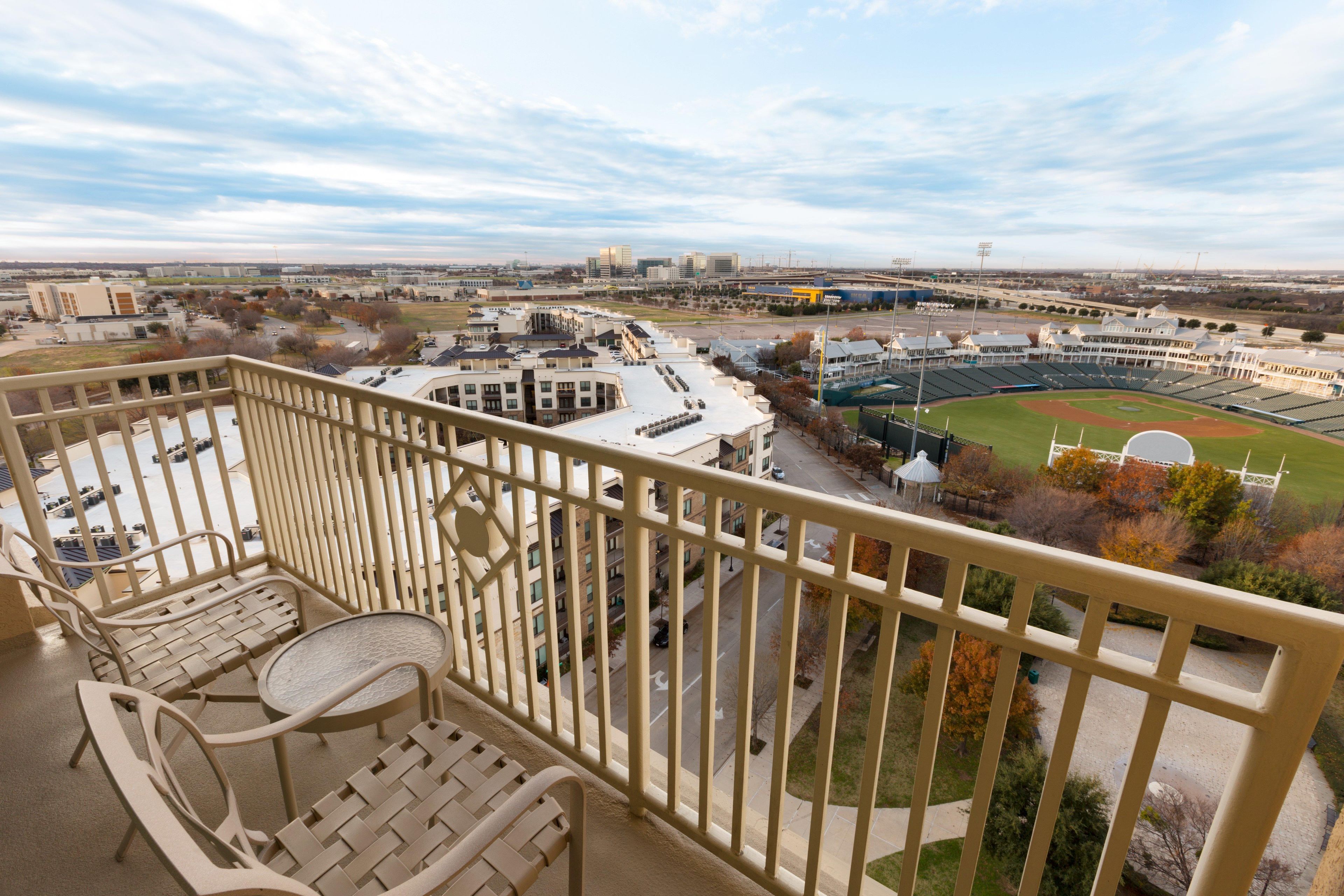 A balcony with a view of a baseball field, buildings, and a parking lot.