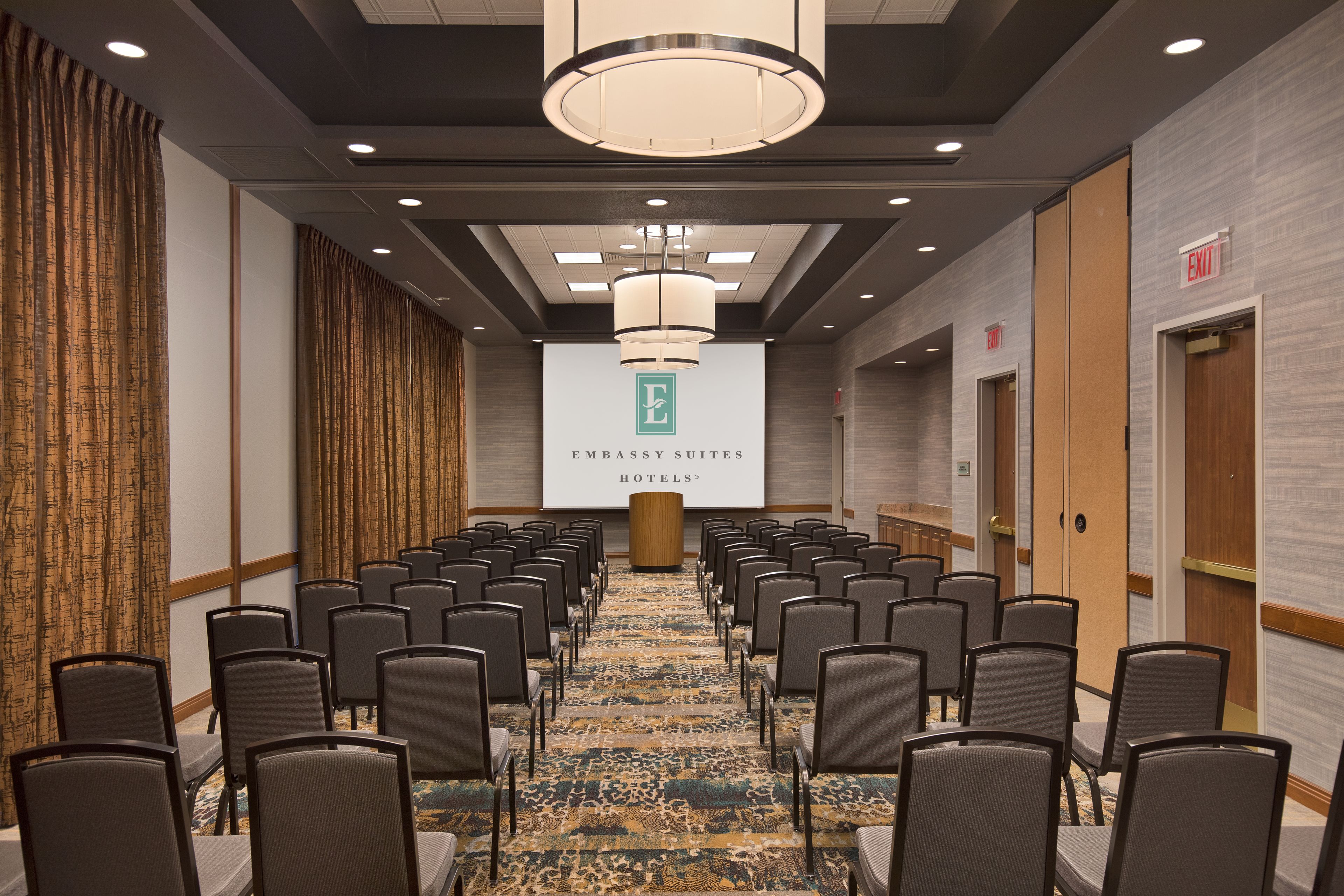 A conference room with rows of chairs, a patterned carpet, and a large banner with the logo of Embassy Suites Hotels.