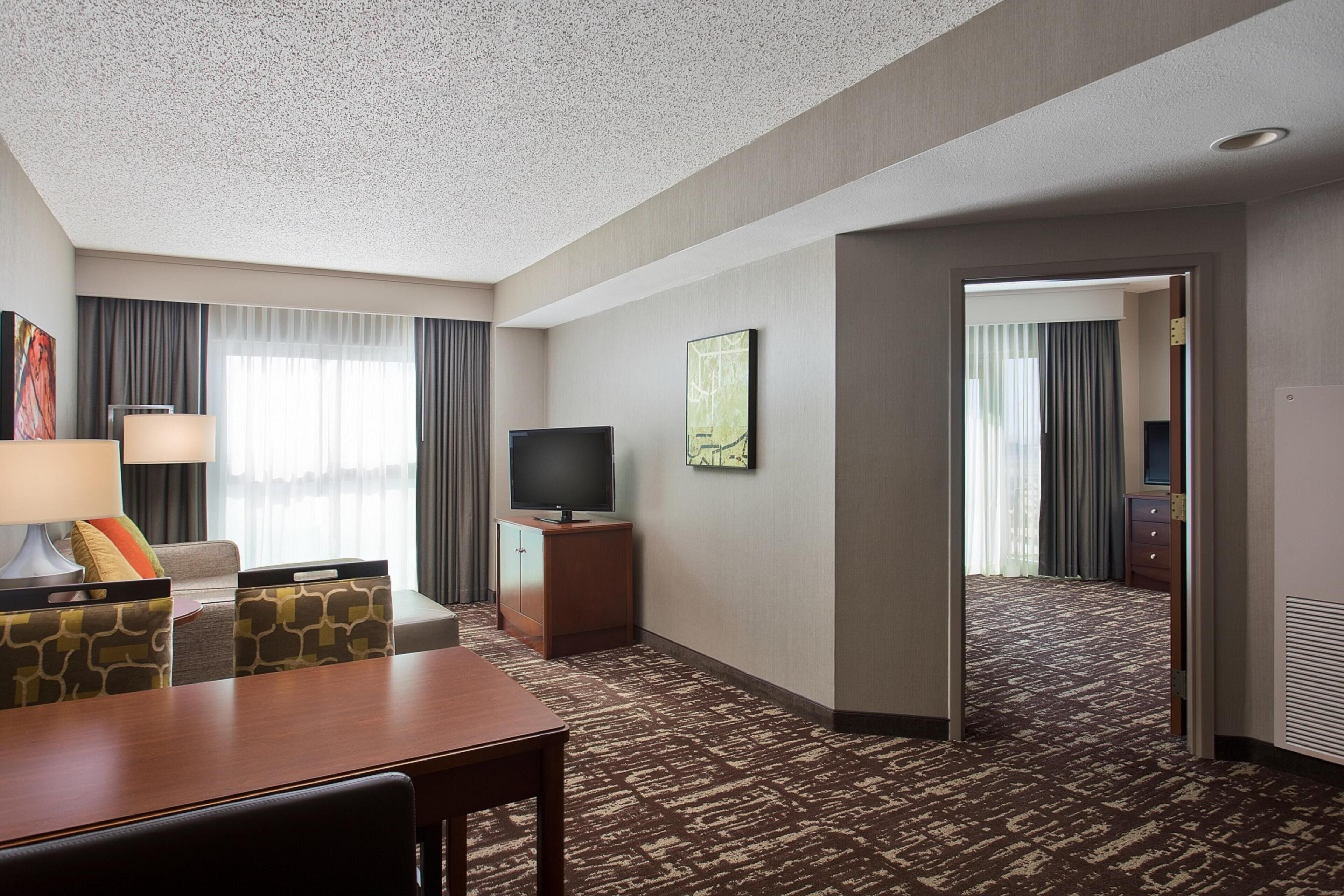 Una habitación de hotel con una mesa de comedor, televisión, sofá y piso alfombrado.