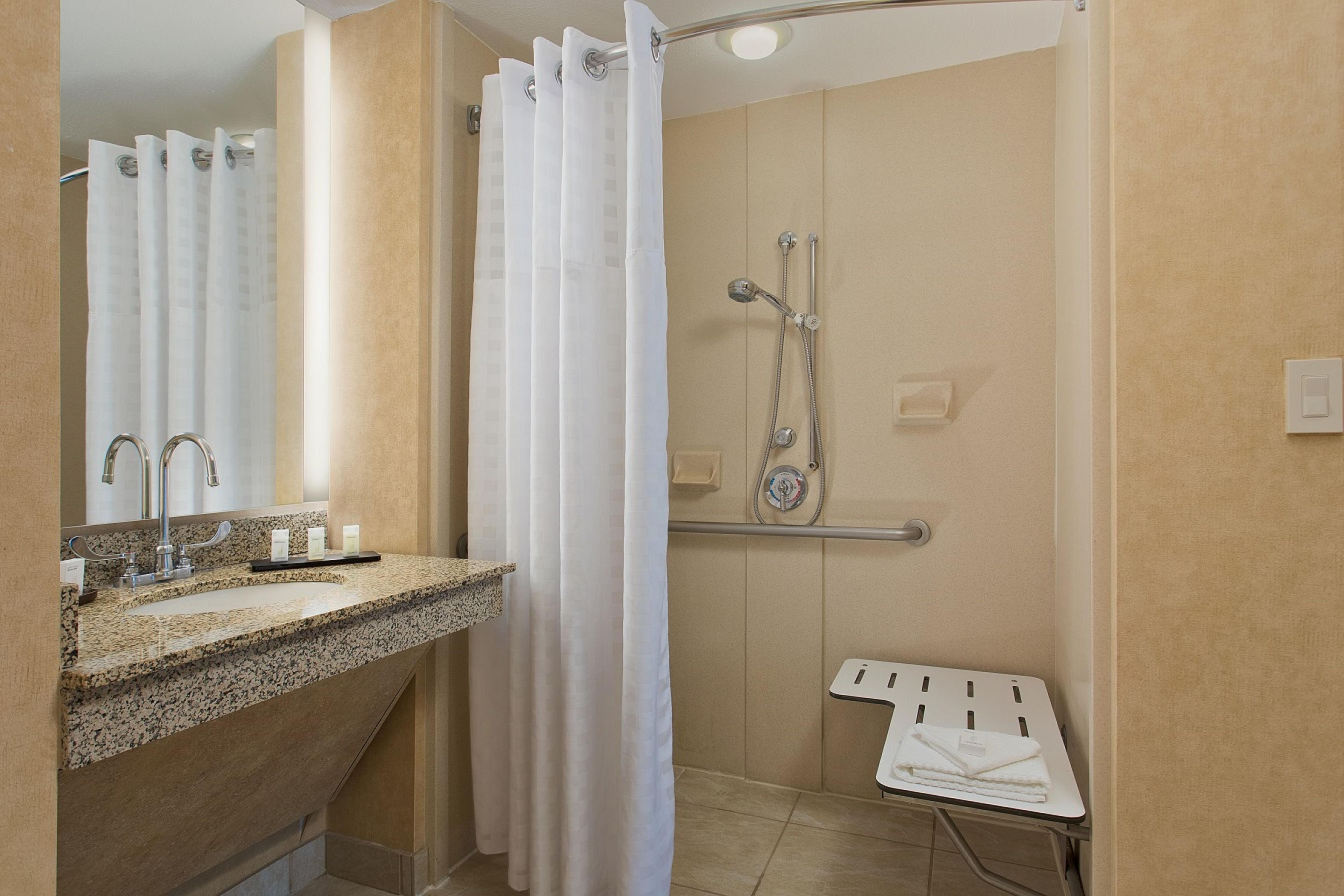 Un baño con lavamanos de encimera de granito, ducha con cabezal de ducha de mano y toallero.