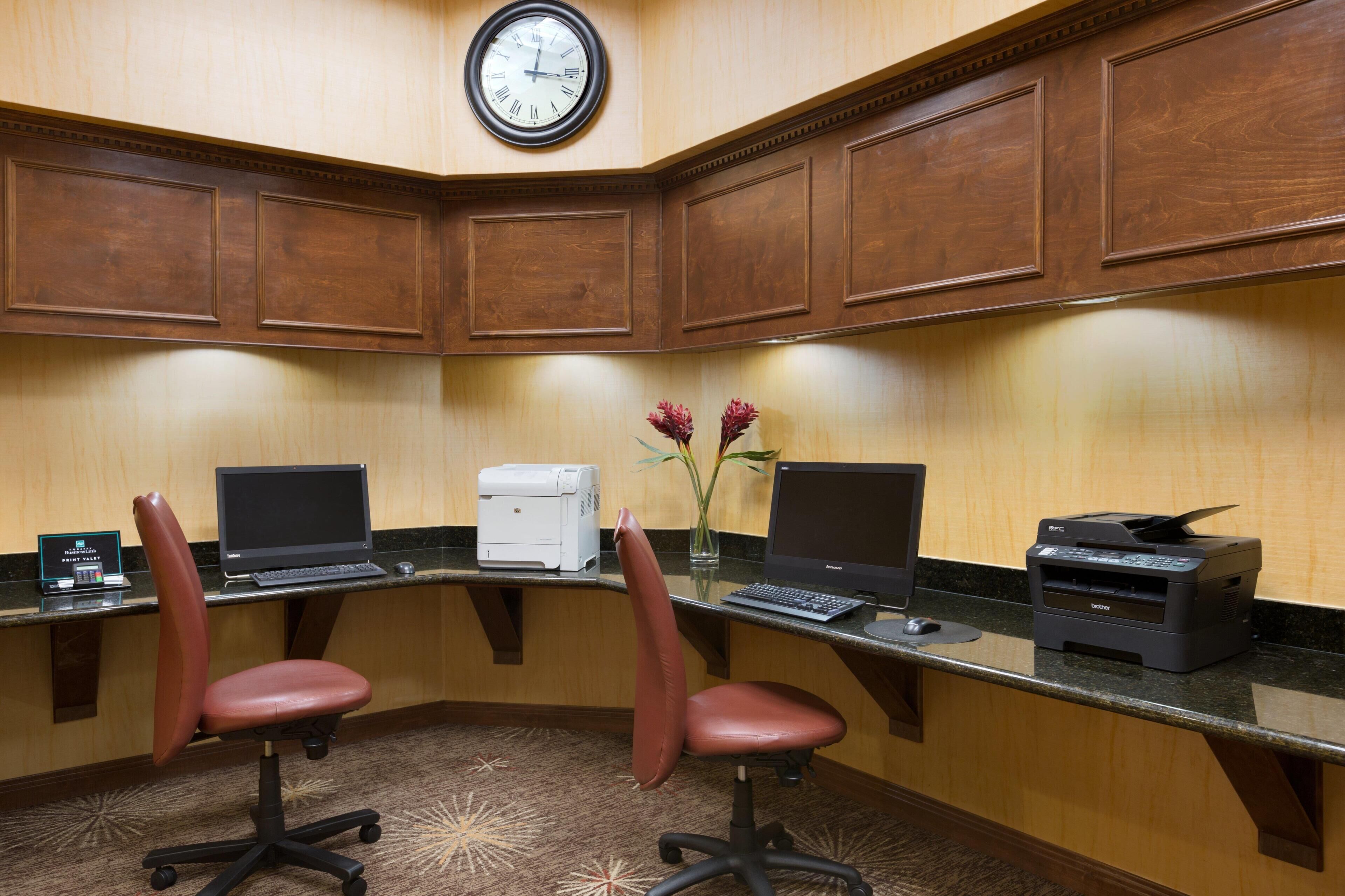 A corner office with two desks, two chairs, a clock, and a printer.