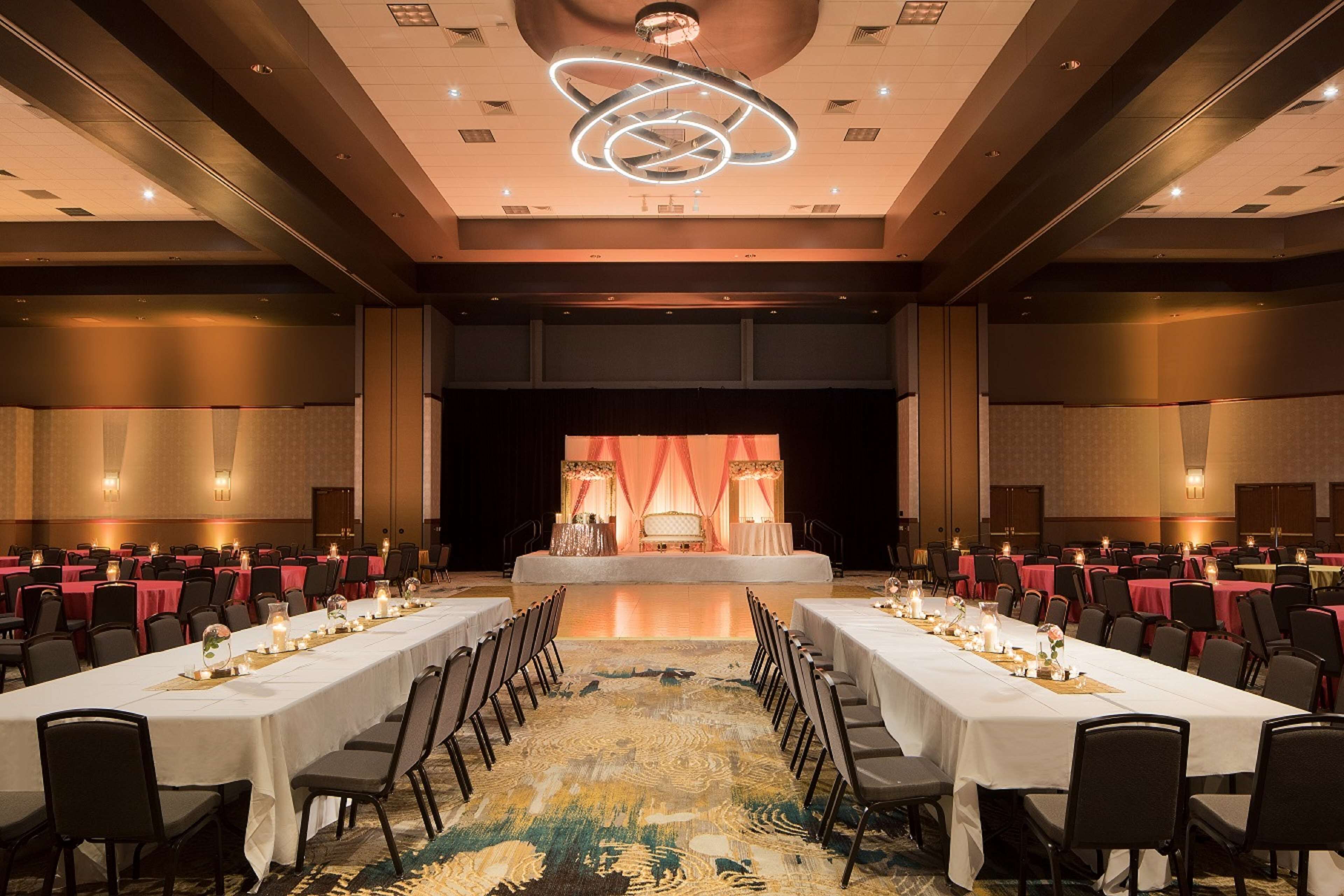 A large conference room with long tables, chairs, and a stage with curtains.