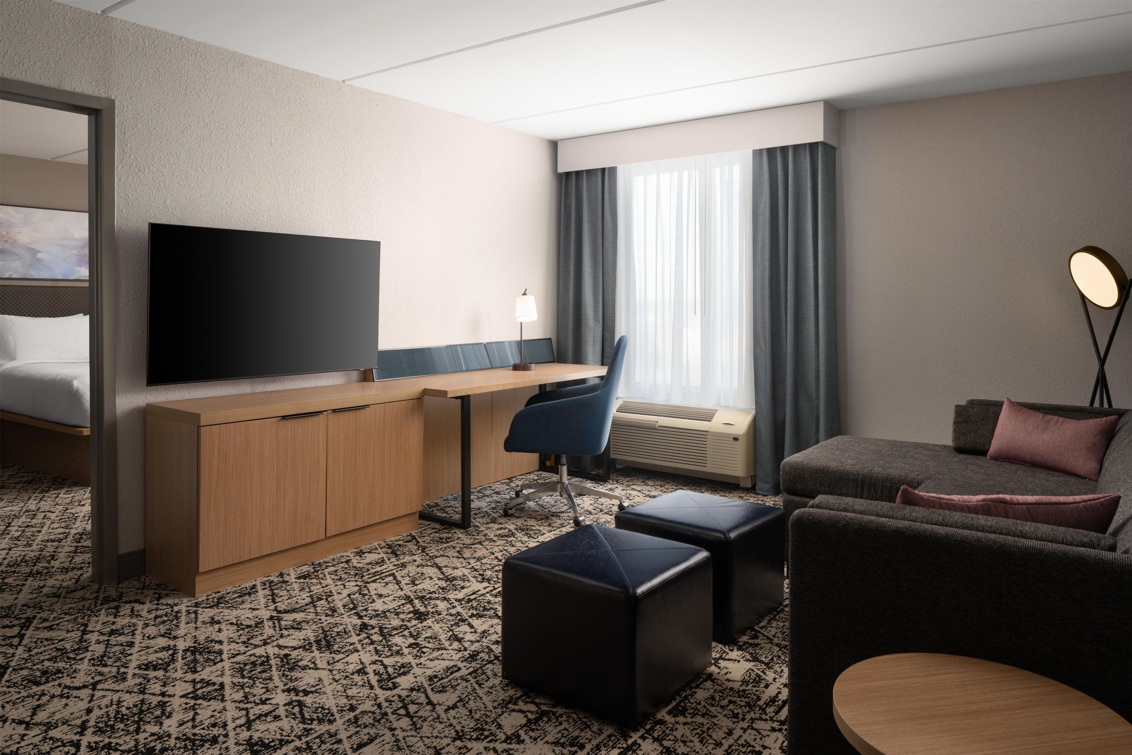 A hotel room with a bed, a desk with a chair, a television, a sofa, and a small round table.
