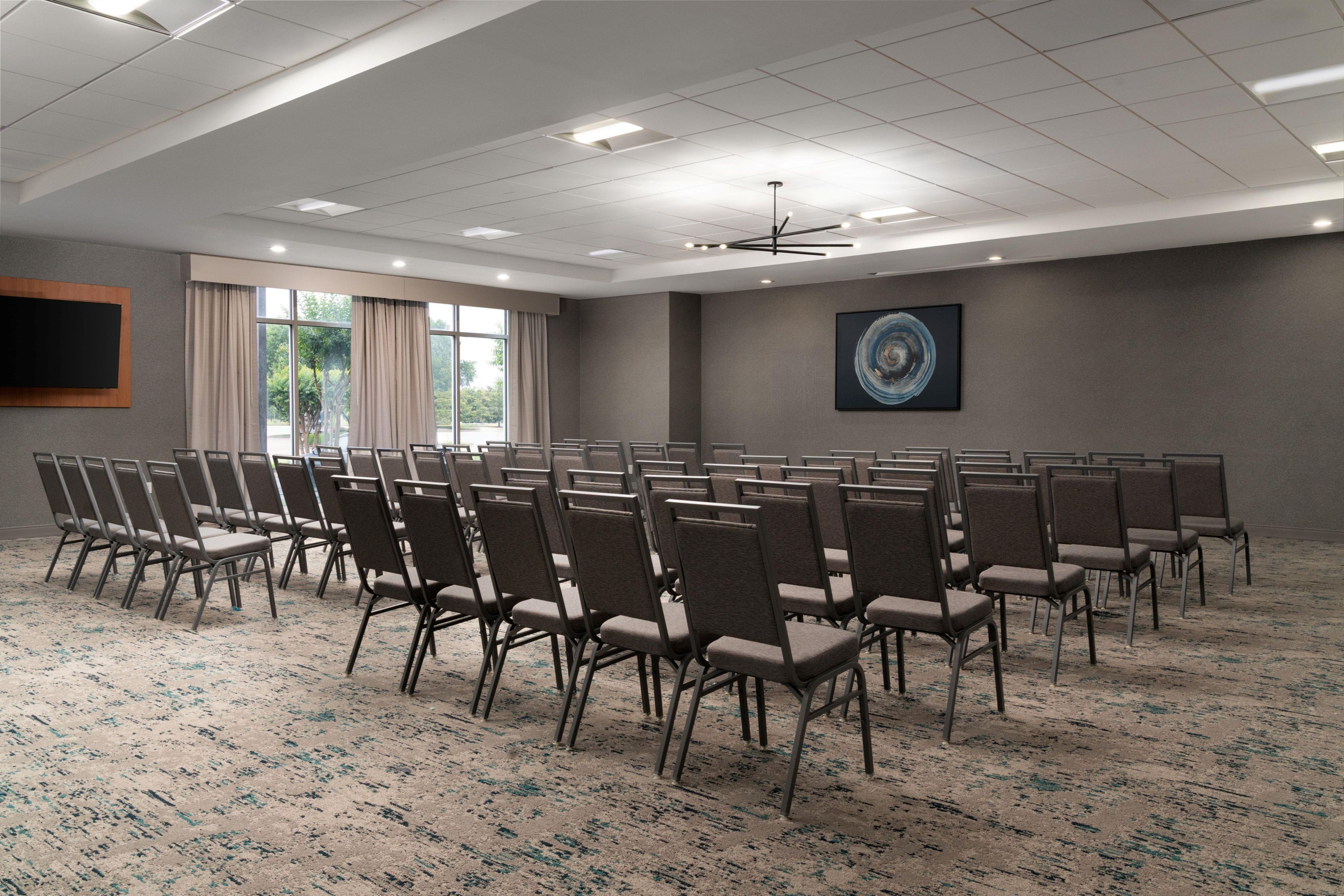 A conference room with rows of chairs, a large screen, and a painting on the wall.
