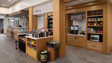 A hotel lobby with a self-service kiosk, a coffee station, and a snack bar.