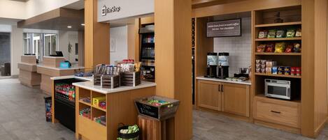 A hotel lobby with a self-service kiosk, a coffee station, and a snack bar.