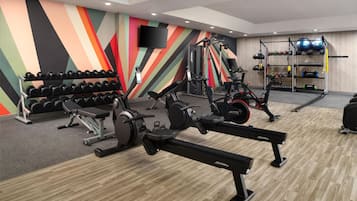 A gym with cardio machines, dumbbells, and a wall-mounted TV.