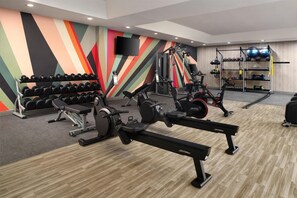 Un gimnasio con máquinas de cardio, pesas y un televisor montado en la pared.