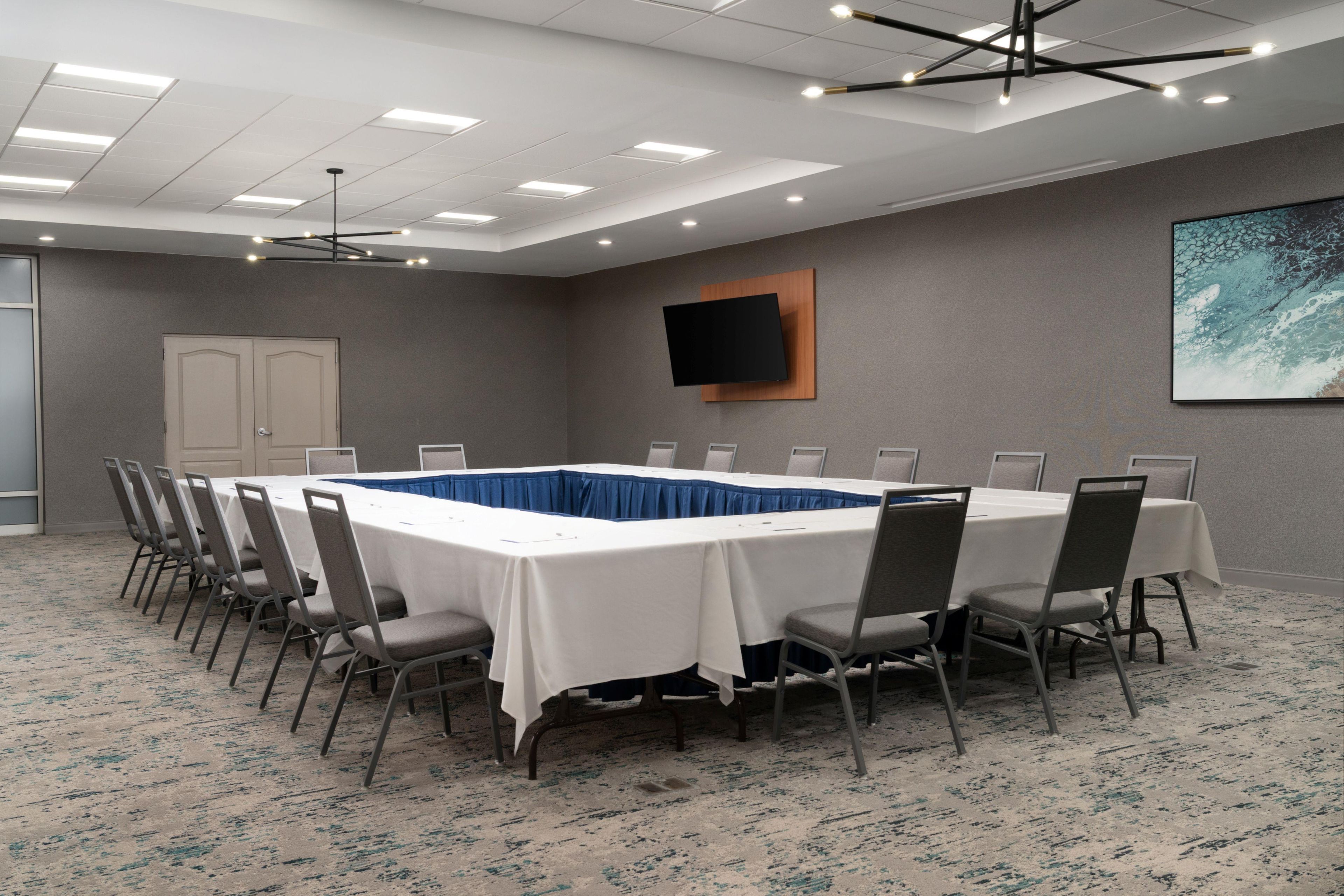 A conference room with a long table, chairs, a flat-screen TV, and a ceiling with recessed lighting.