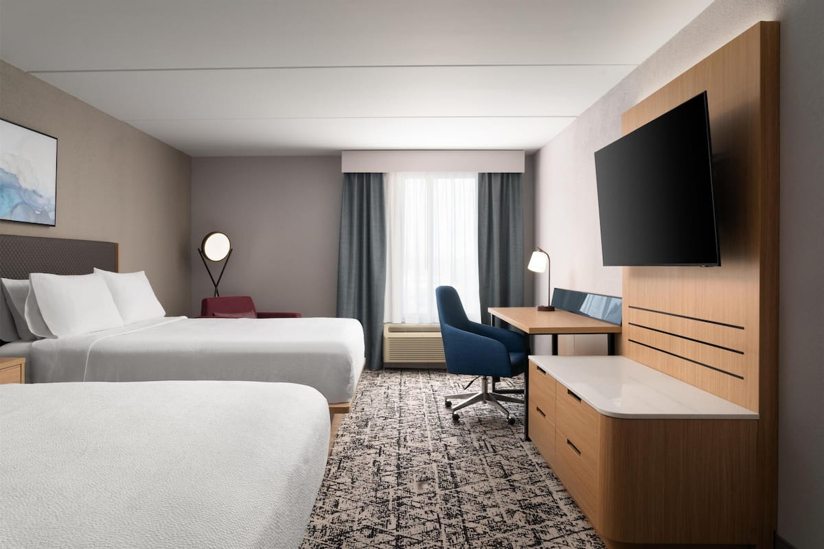 Habitación de hotel con dos camas, un escritorio, una silla, un televisor y una ventana con cortinas.
