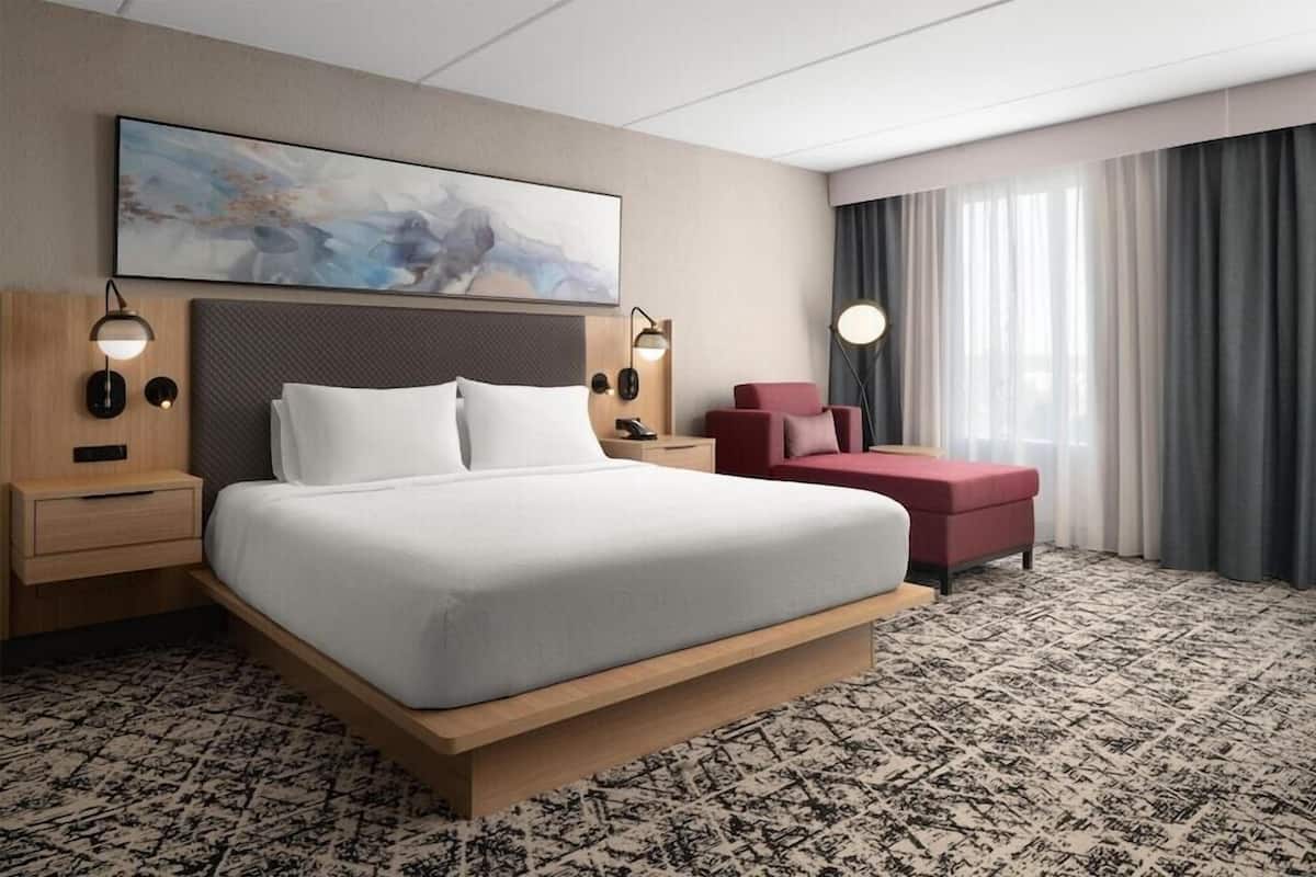 Una habitación de hotel con una cama grande, un sillón rojo, un escritorio y un cuadro en la pared.