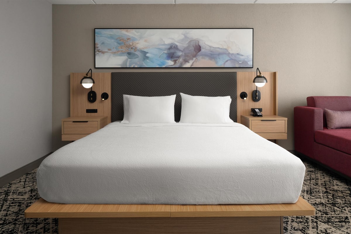 Habitación de hotel con una cama grande, dos mesitas de noche, un cabecero y una obra de arte colgada en la pared.