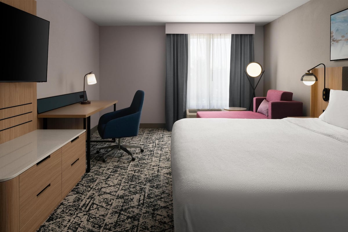 Habitación de hotel con cama, escritorio, silla, televisor y dos lámparas de noche.