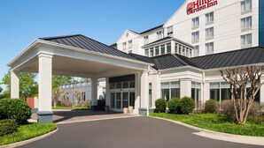 Een Hilton Garden Inn met een overdekte ingang, grote ramen en een heldere lucht.