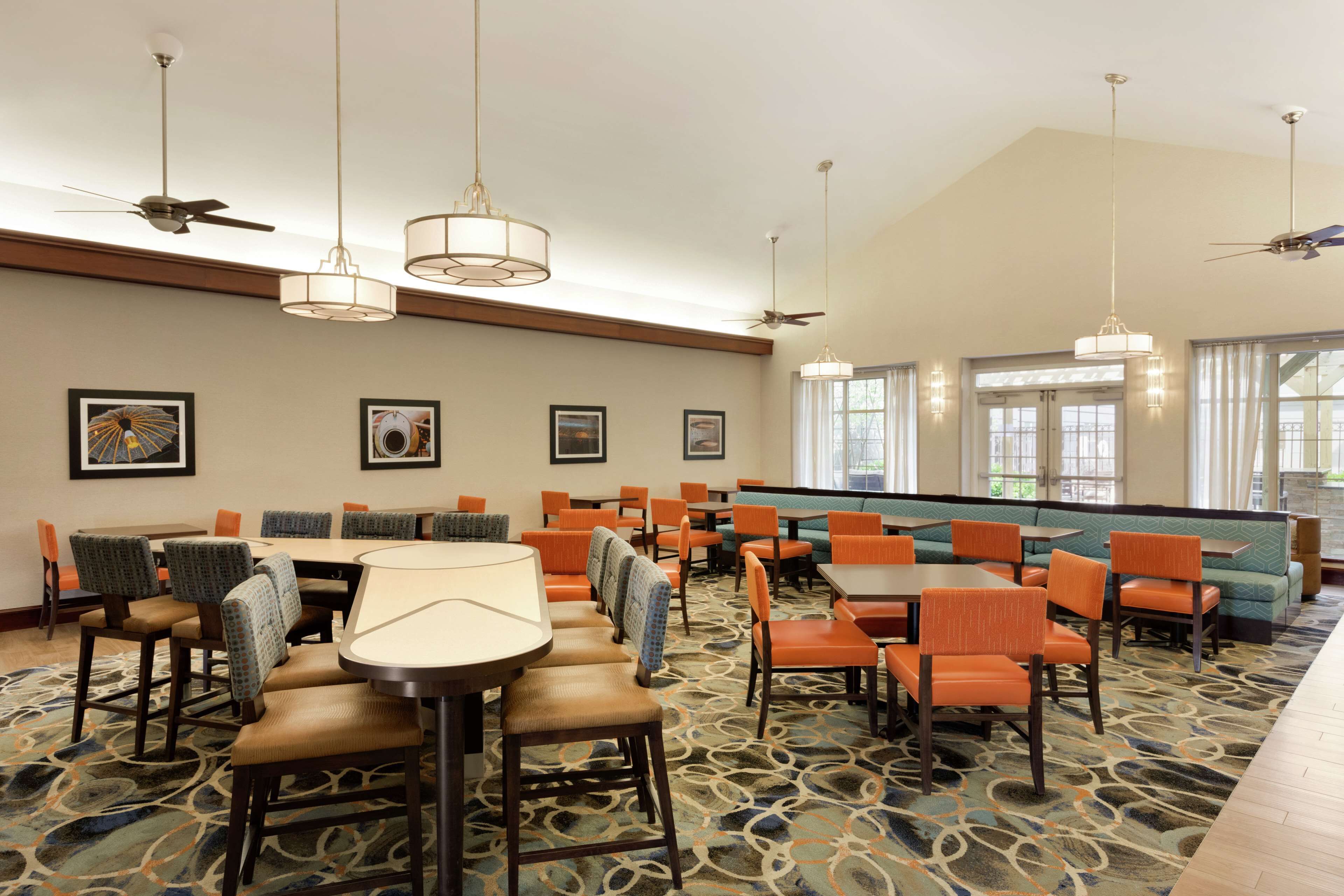 A hotel dining area with multiple tables and chairs, ceiling fans, and framed artwork on the walls.