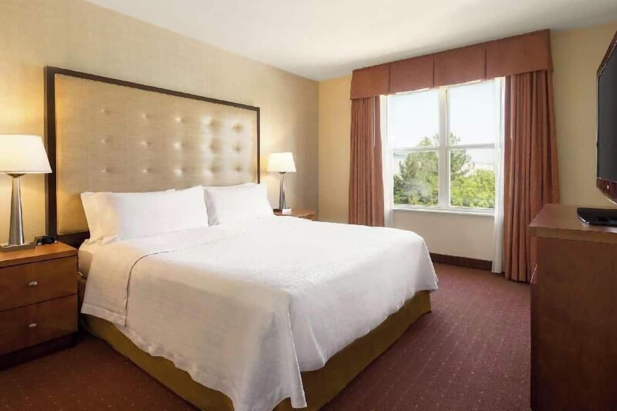 Ein Hotelzimmer mit einem großen Bett, zwei Nachttischen mit Lampen, einem Schminktisch und einem Fenster mit Vorhängen.