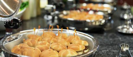 A buffet setup with several metal serving trays containing food items.