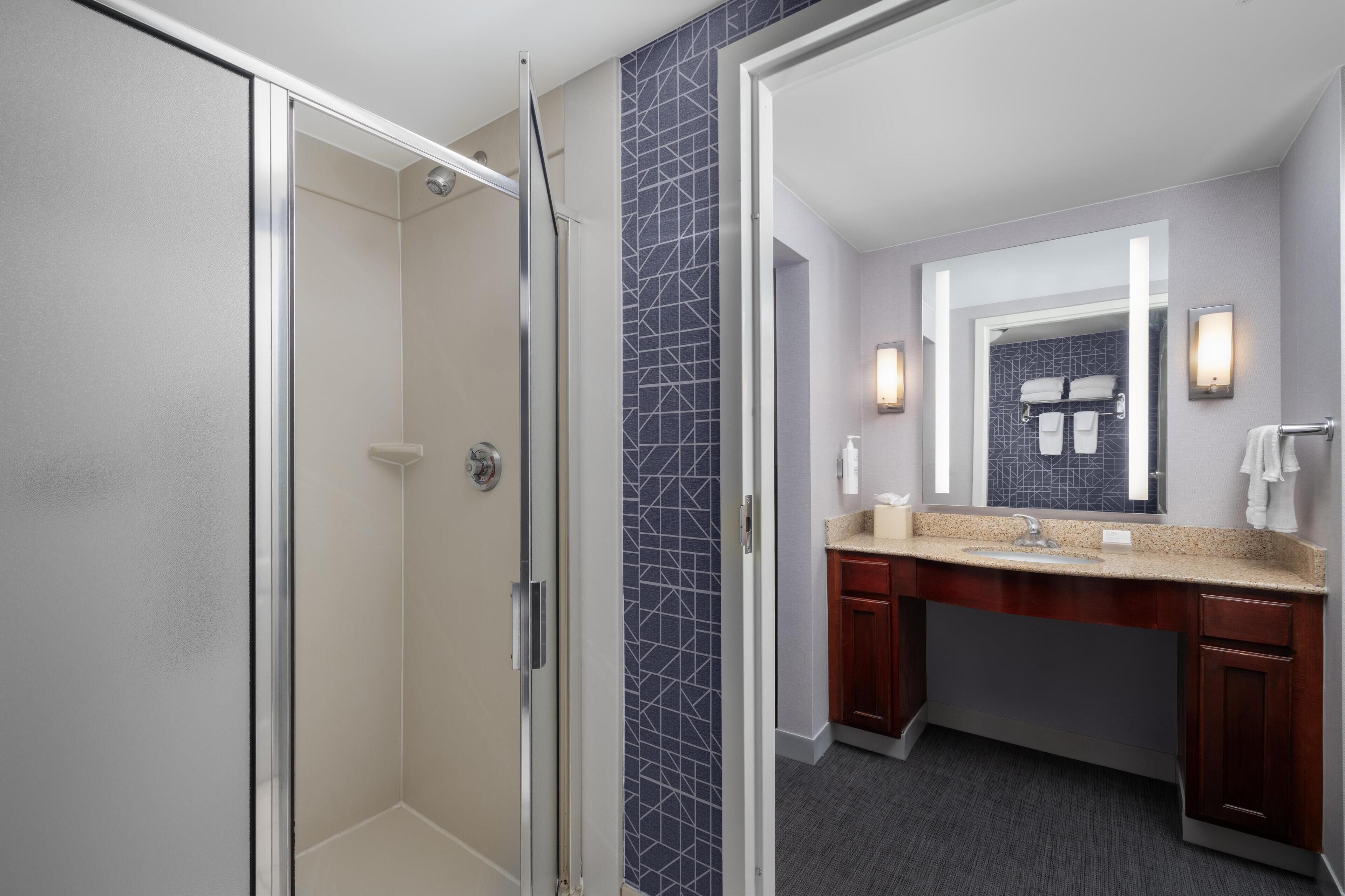A modern bathroom with a glass shower enclosure, a vanity with a granite countertop, and a large mirror.