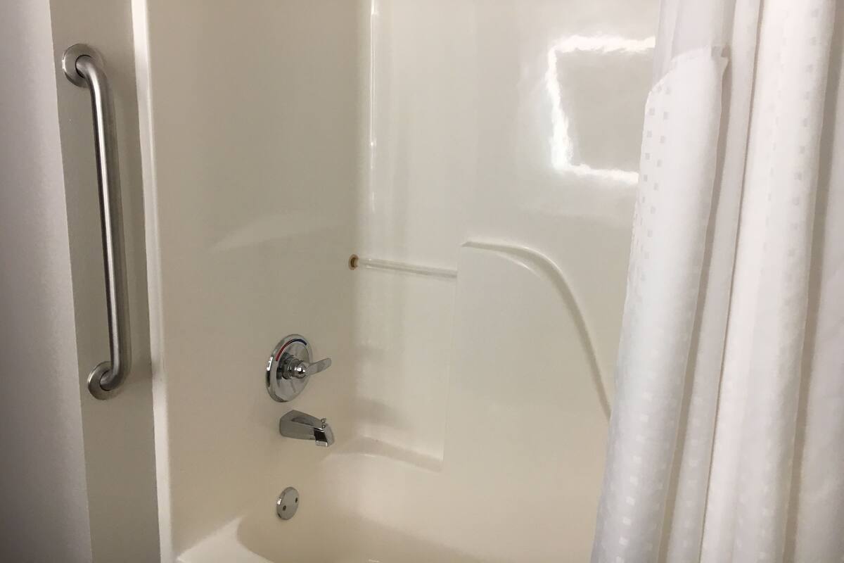 A bathroom with a white bathtub, a shower area, and a handrail.