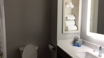 A bathroom with a toilet, a sink, and a mirror. There are towels and toiletries on the sink counter.