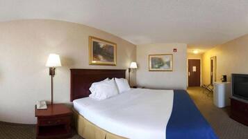 Habitación de hotel con una cama grande, dos lámparas de noche, un escritorio con teléfono, un televisor y dos cuadros en la pared.