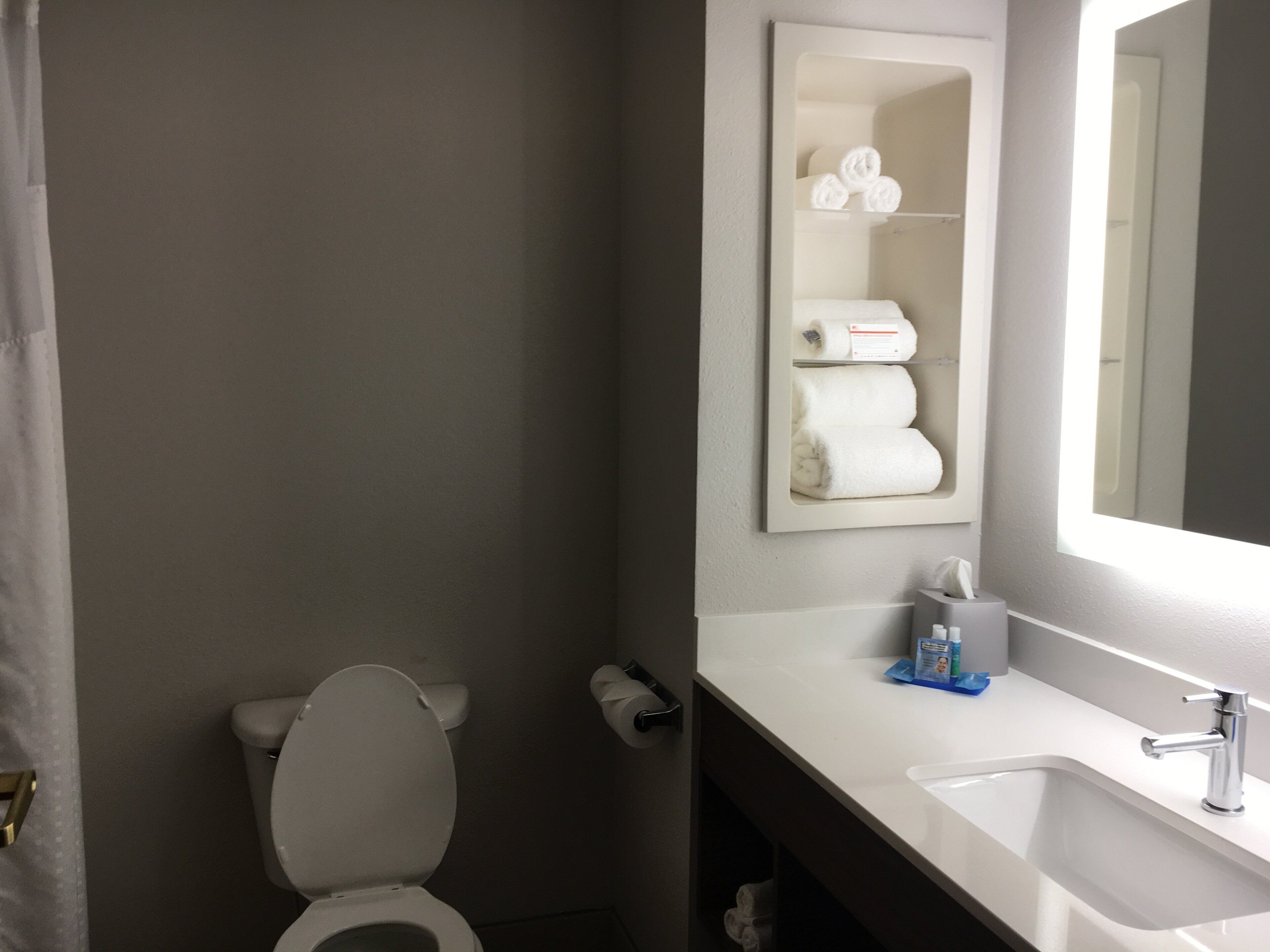A bathroom with a toilet, a sink, a mirror, and a towel rack with towels.