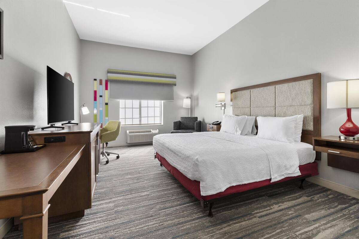 A hotel room with a large bed, a desk with a computer, a TV, and a chair.