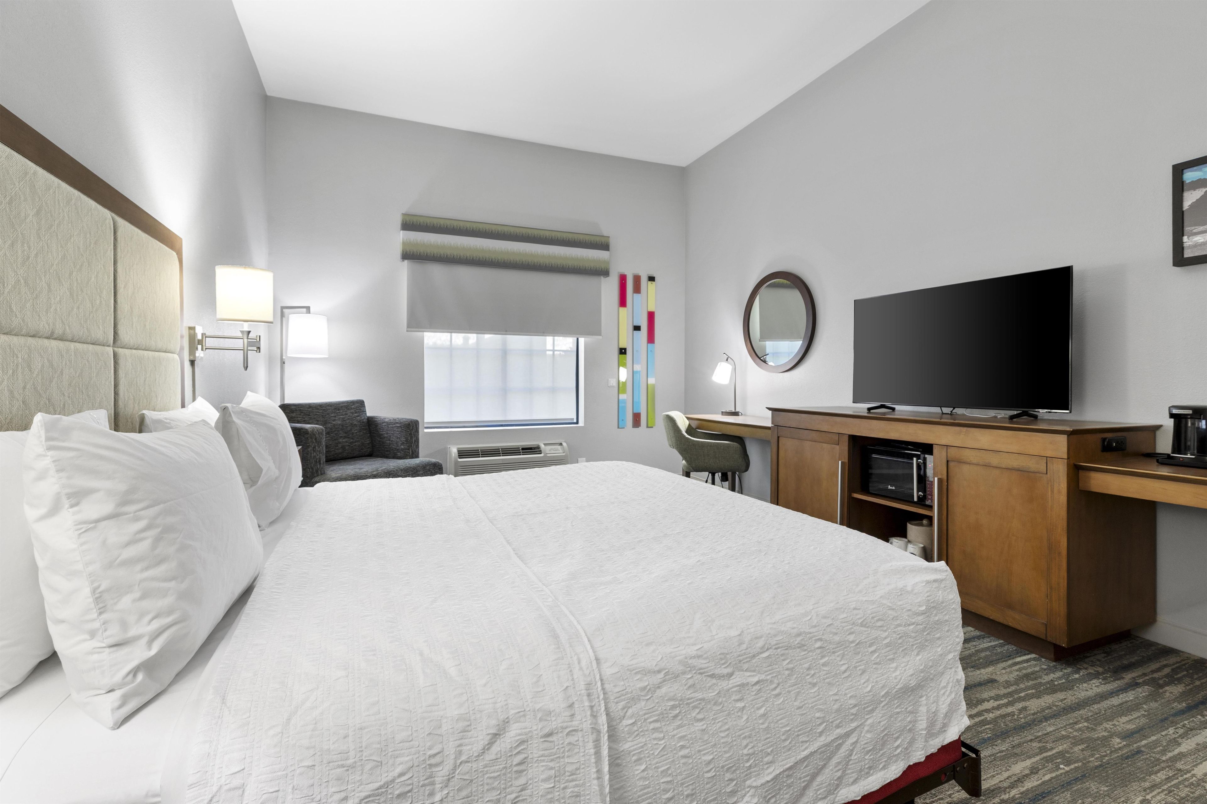 A hotel room with a bed, desk, television, and a window with blinds.