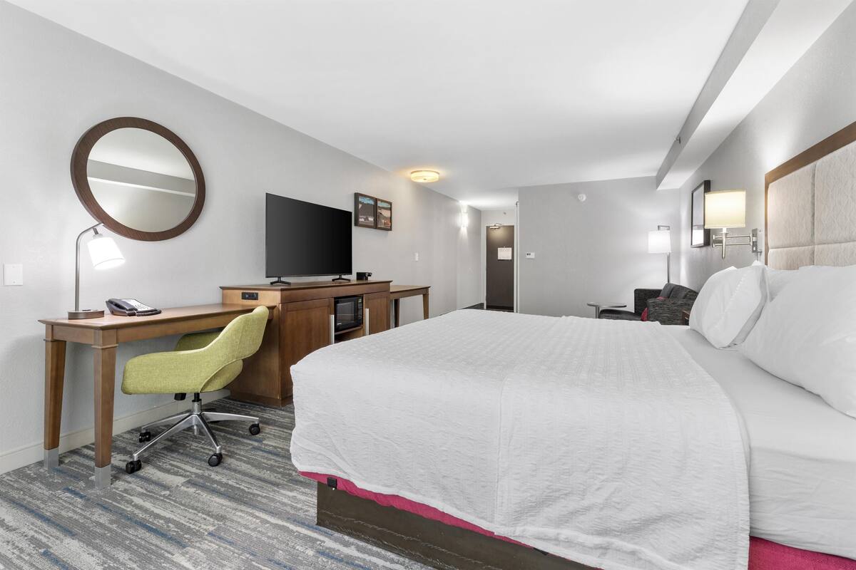 A hotel room with a bed, desk, chair, TV, and a mirror.