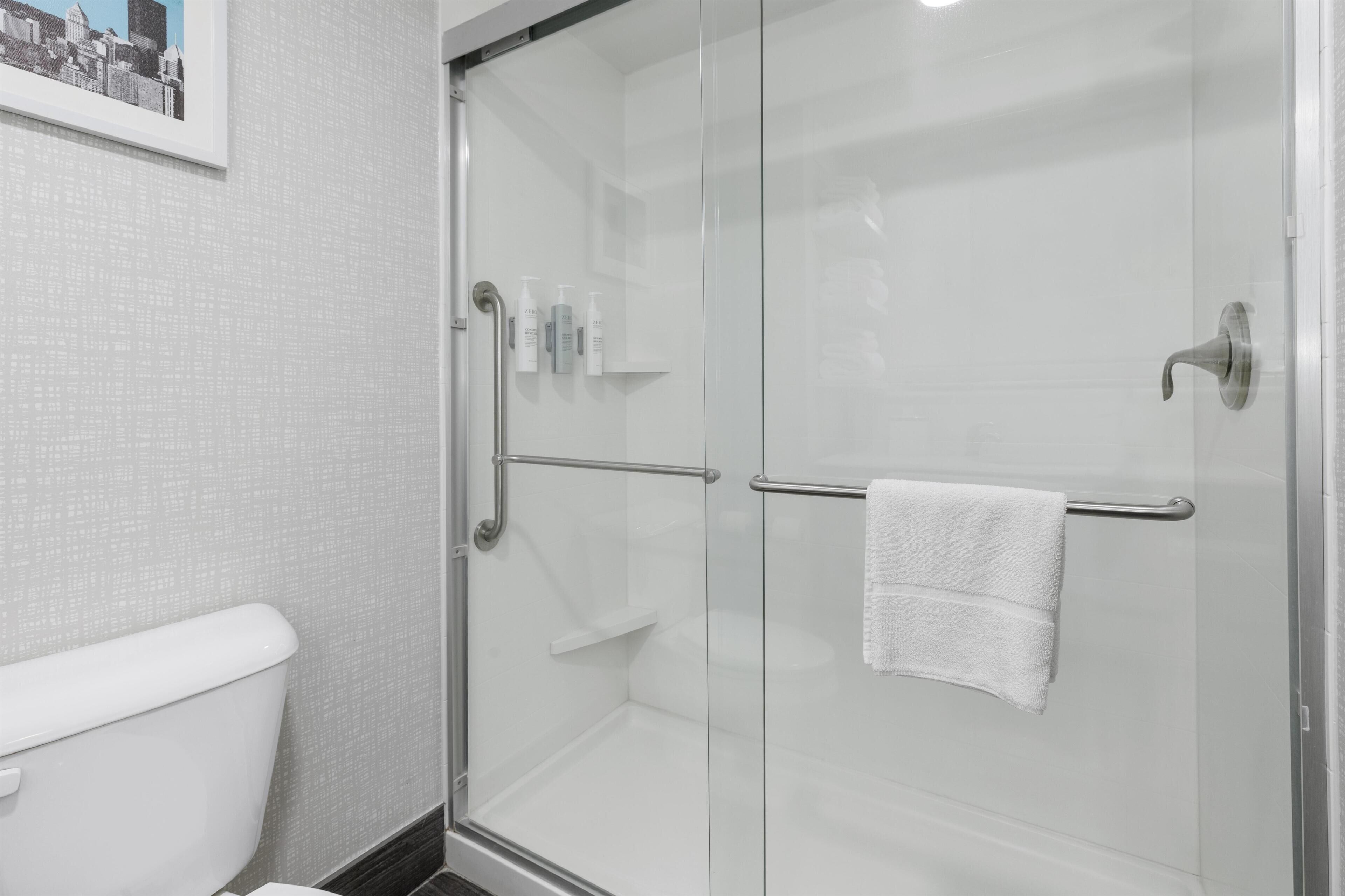 A modern bathroom with a glass shower enclosure, a white toilet, and a framed cityscape picture on the wall.