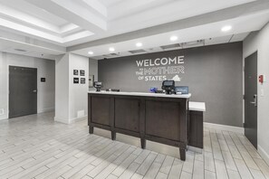 A reception area with a 'Welcome to the Mother of States' sign, a reception desk, and a door in the background. - Hampton Inn Salem, VA (Salem)