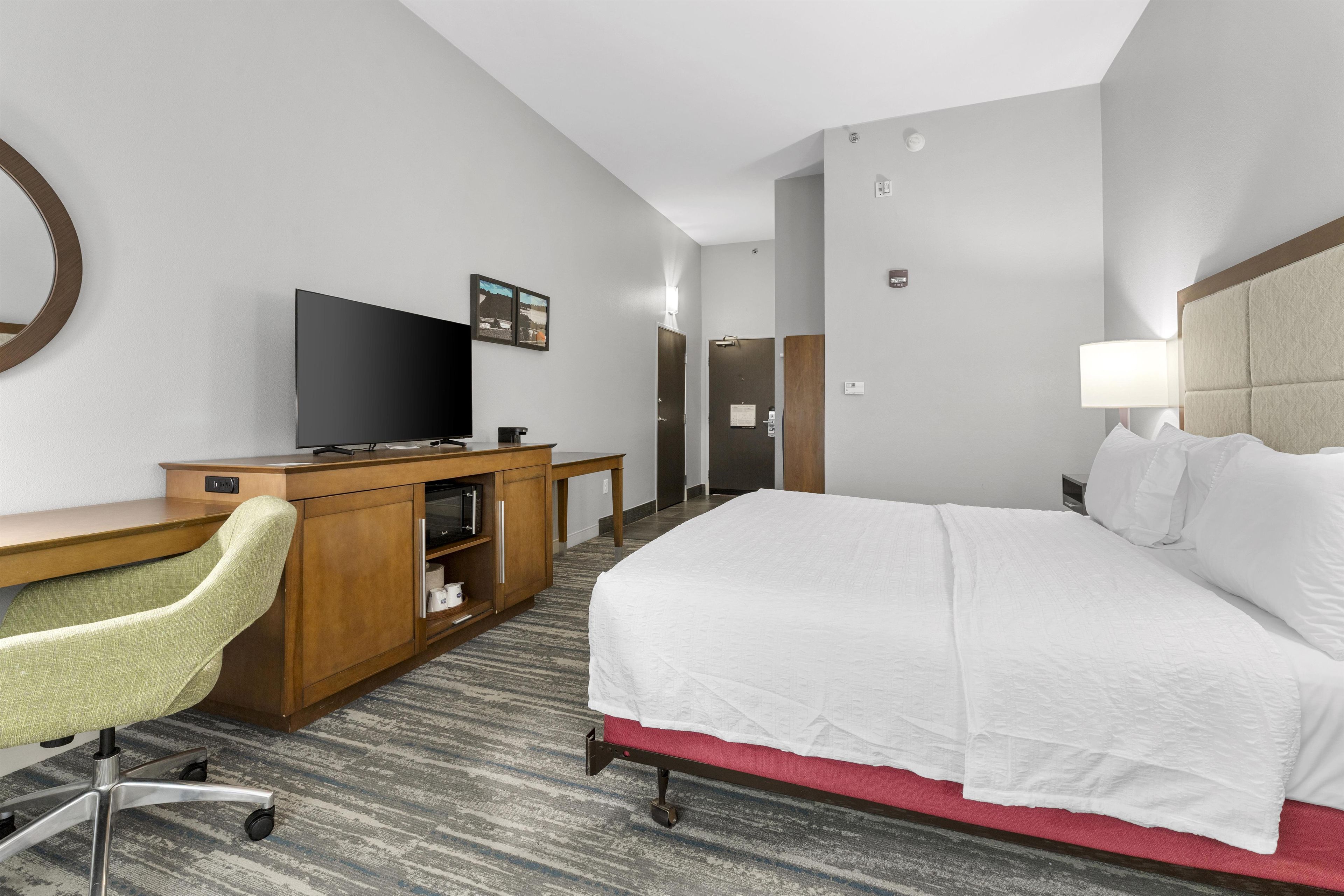Ein Hotelzimmer mit Bett, Schreibtisch, Stuhl, Fernseher und einer Tür zum Badezimmer.