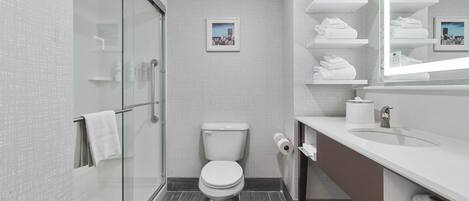 Un baño moderno con cabina de ducha de vidrio, inodoro, lavamanos y espejo con toalleros.