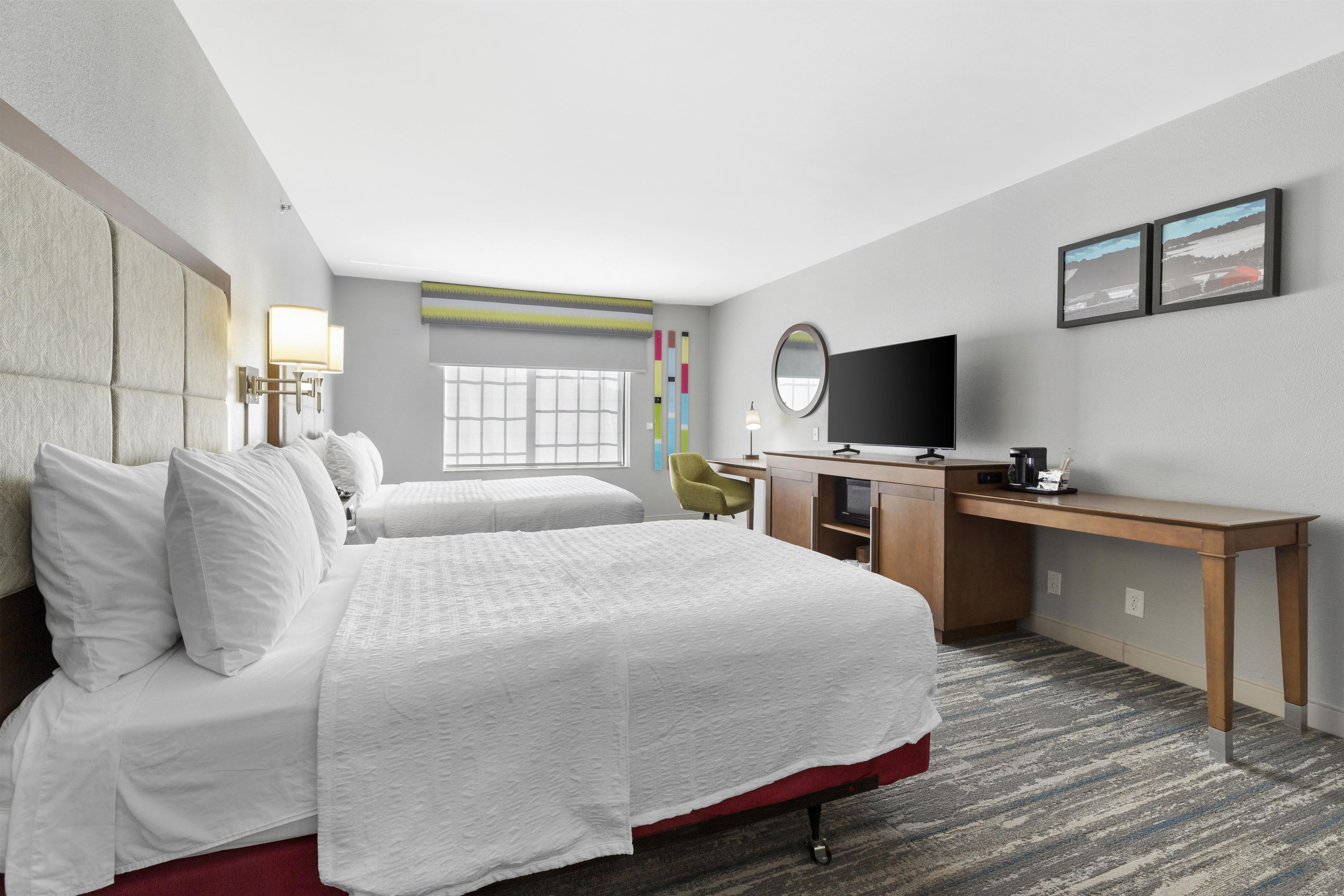 Een hotelkamer met twee bedden, een bureau, een televisie en een raam.