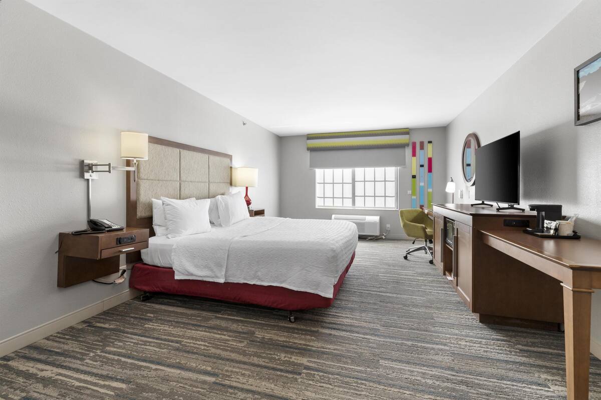 A hotel room with a bed, desk, chair, and TV.