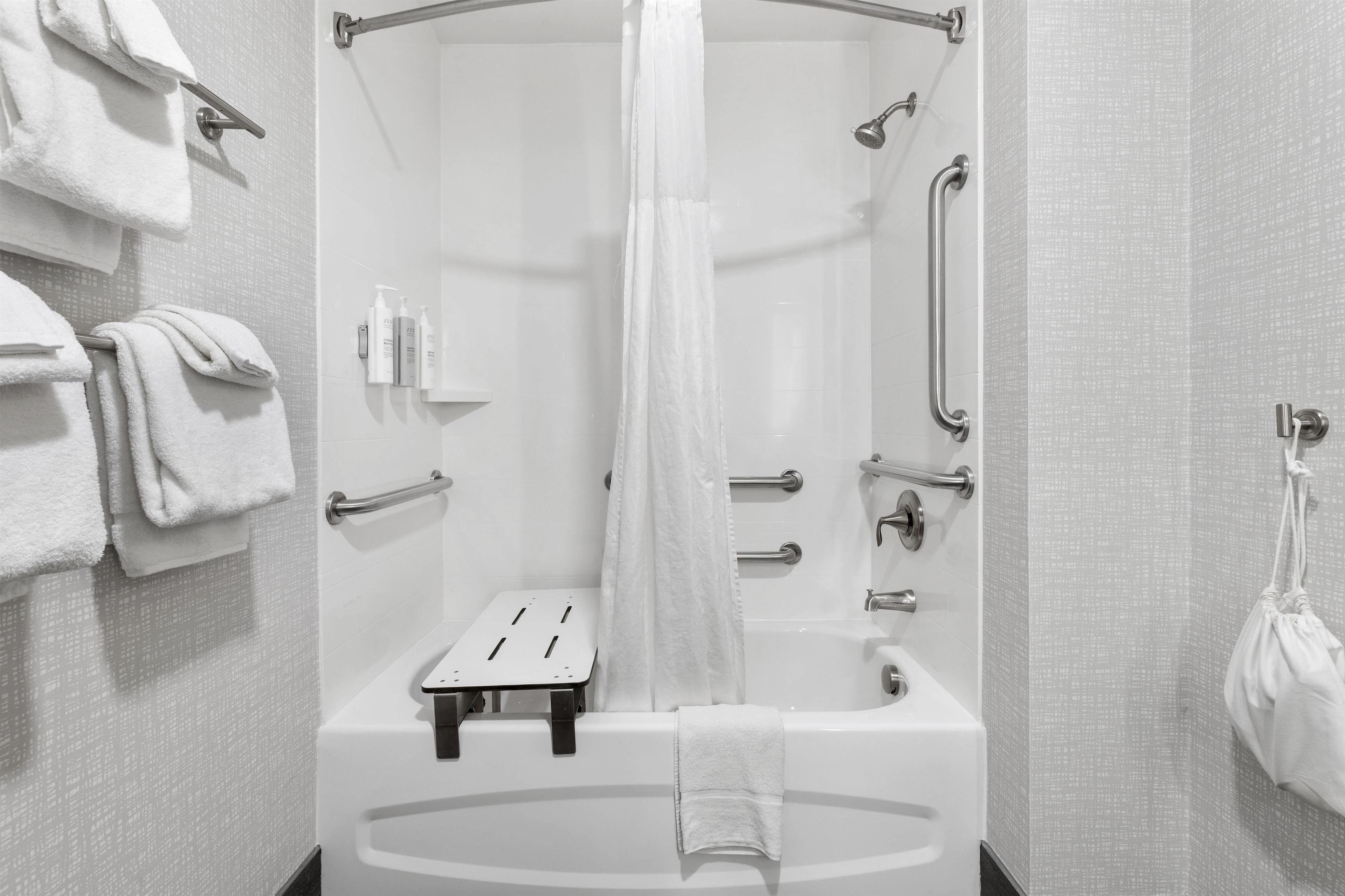 A modern bathroom with a walk-in shower, grab bars, a towel rack, and a small shelf with toiletries.