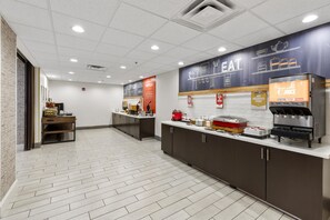 Un área de cocina moderna y limpia con una estación de gofres, un dispensador de jugo y una barra con diversas opciones de comida.