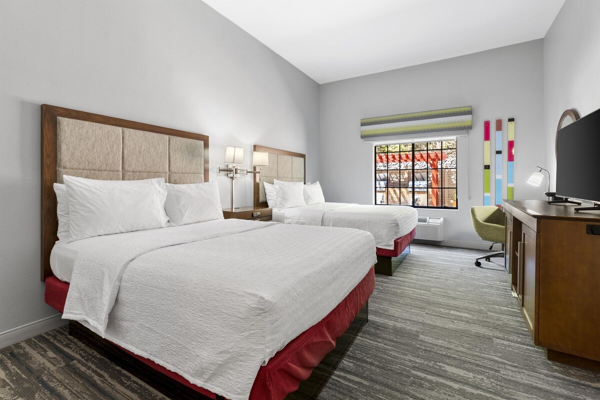 Habitación de hotel con dos camas, un escritorio, una silla y un televisor.