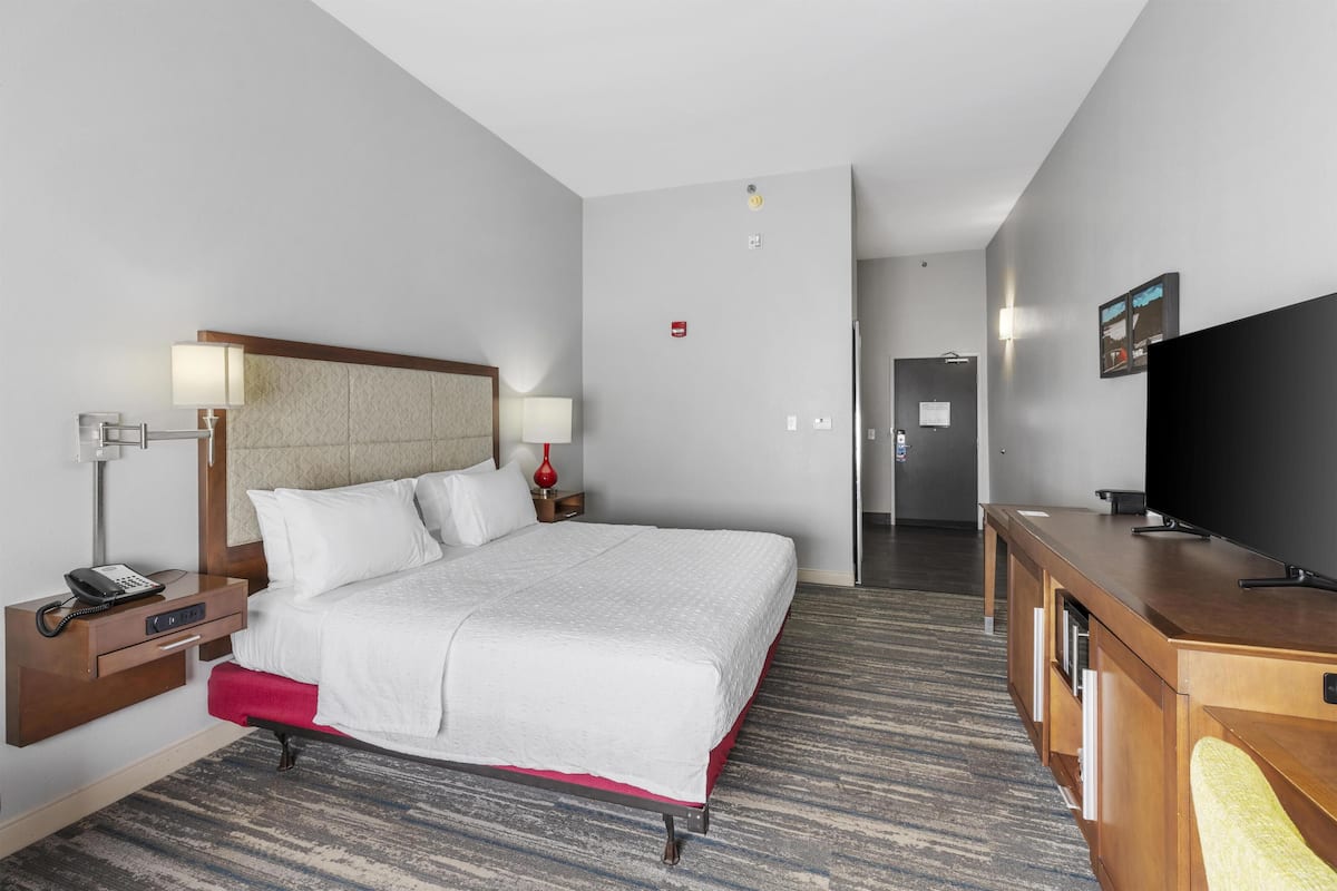 A hotel room with a bed, bedside tables, a desk, a television, and a carpeted floor.