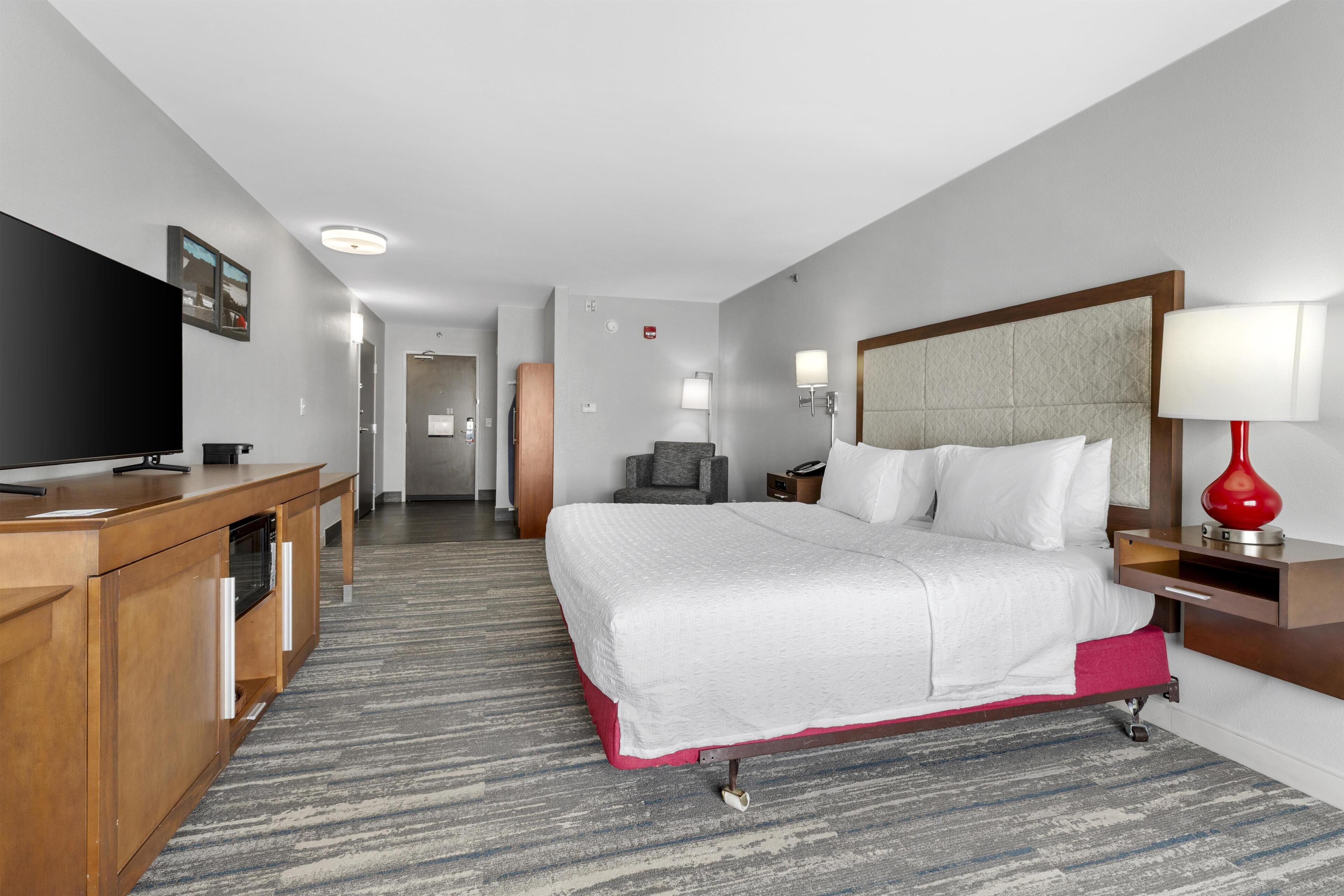 A hotel room with a bed, a TV, a desk, and a red lamp.