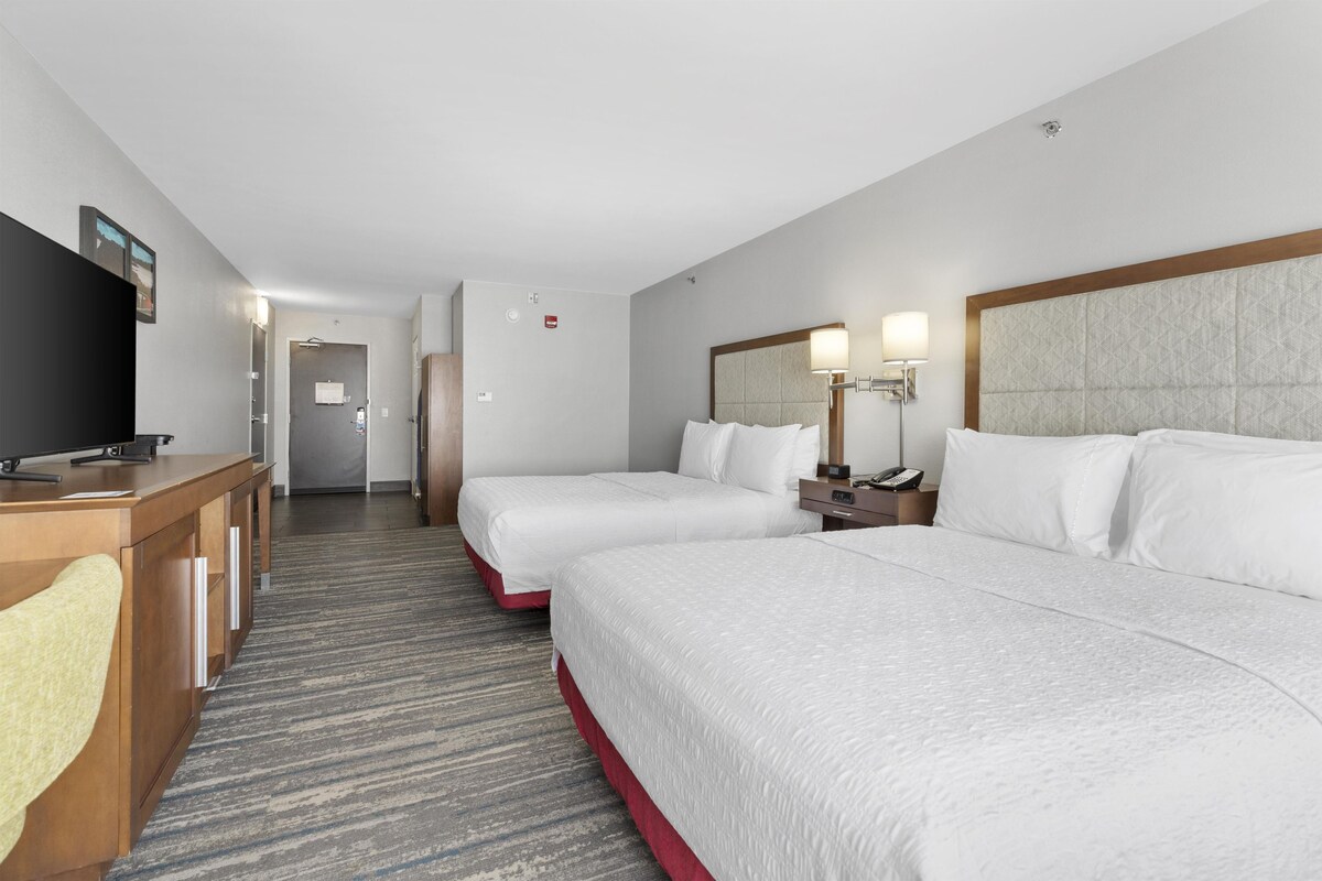 Habitación de hotel con dos camas, un escritorio, un televisor y baño.