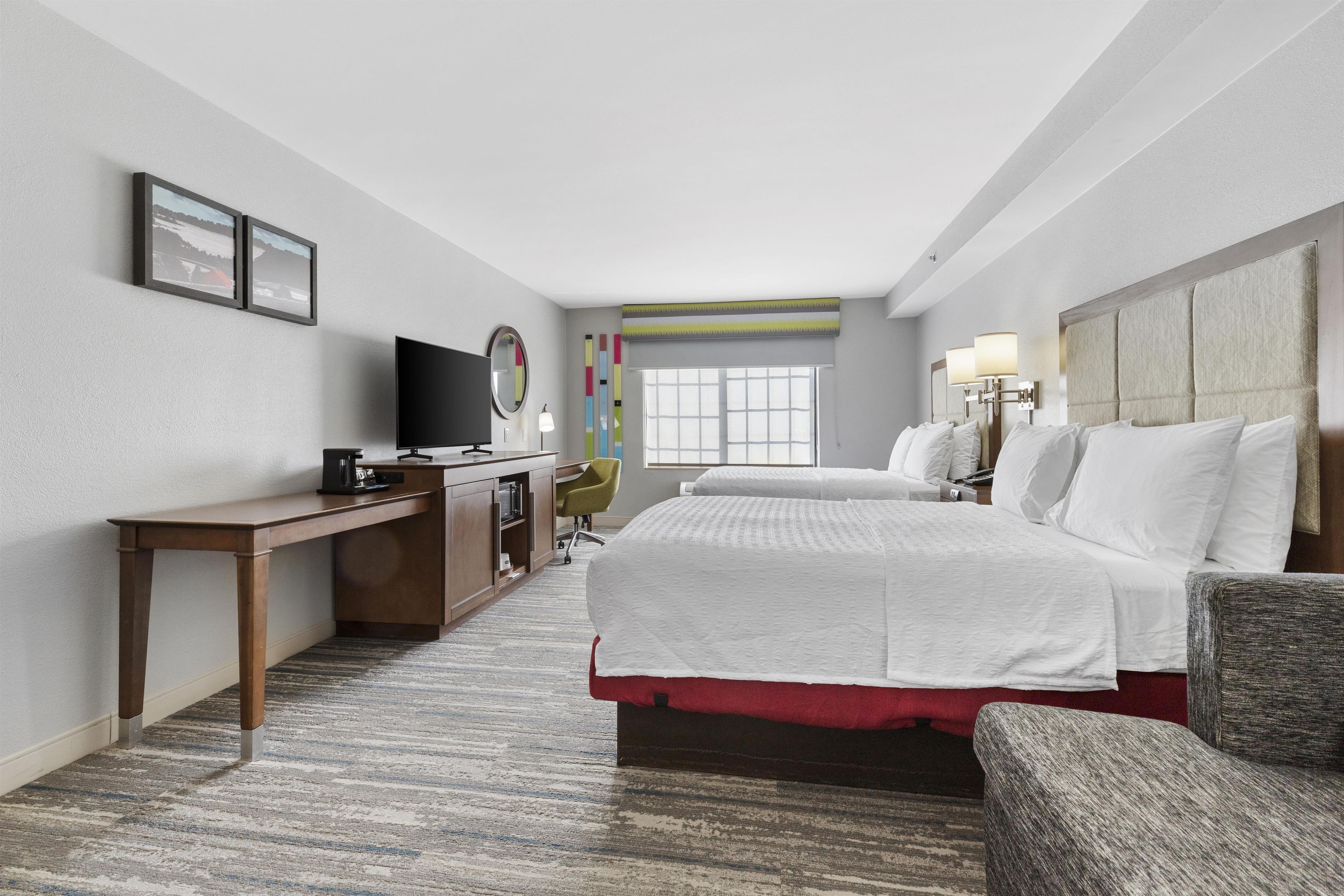 A hotel room with a bed, a desk, a chair, a TV, and a window.