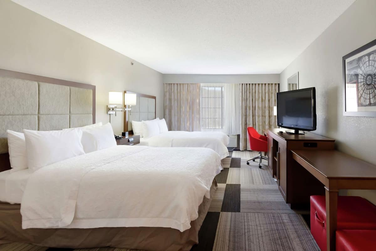 A hotel room with two beds, a desk, a TV, and a red chair.